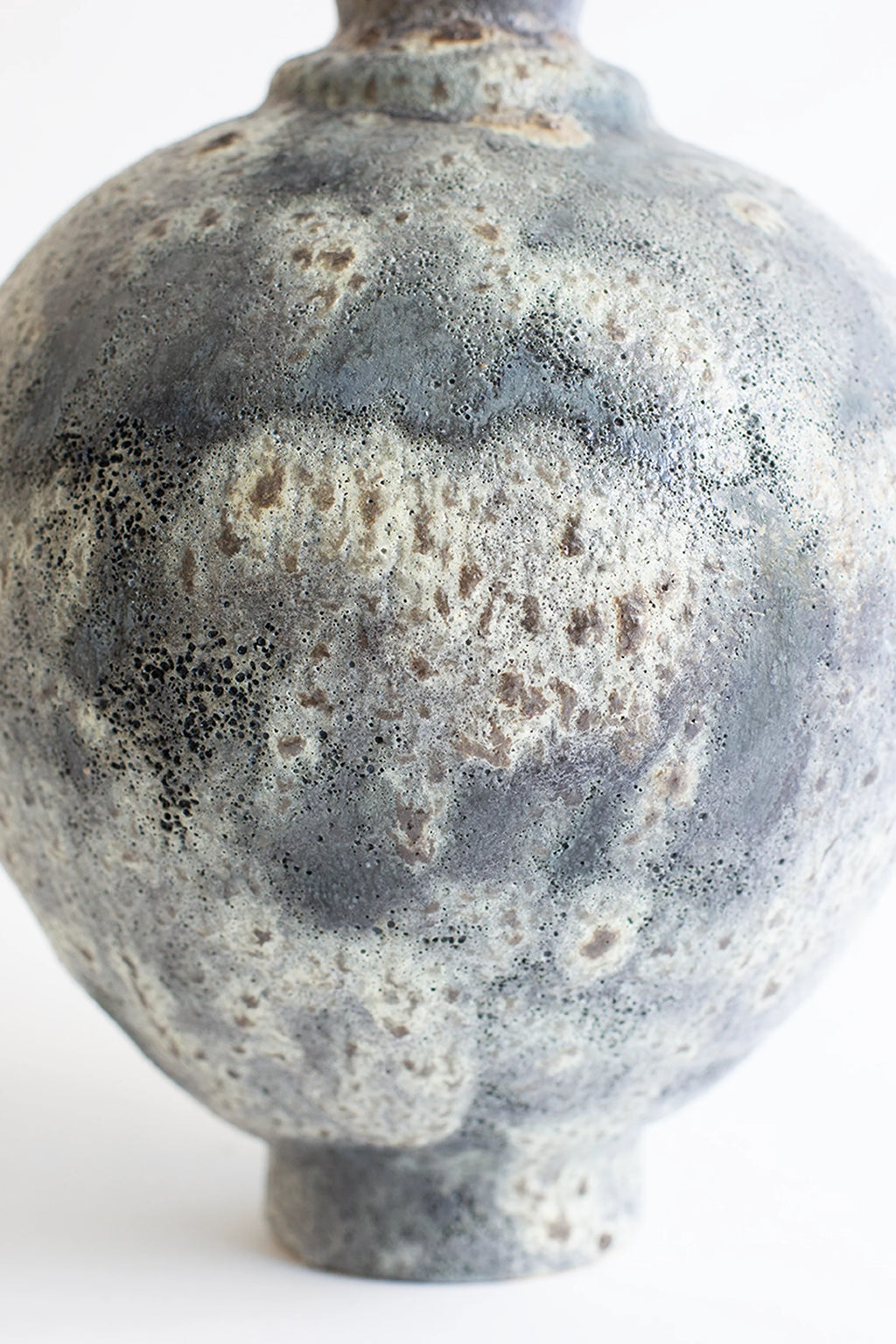 Canoa Lab Ánfora Gecko Vase, a handcrafted ceramic vase featuring a distinctive porous volcanic texture in mottled grey, cream, and earthy brown tones with a globular body and narrow neck. This organic modern stoneware vase is perfect for rustic shelf styling in japandi or wabi-sabi inspired living rooms and bedrooms.