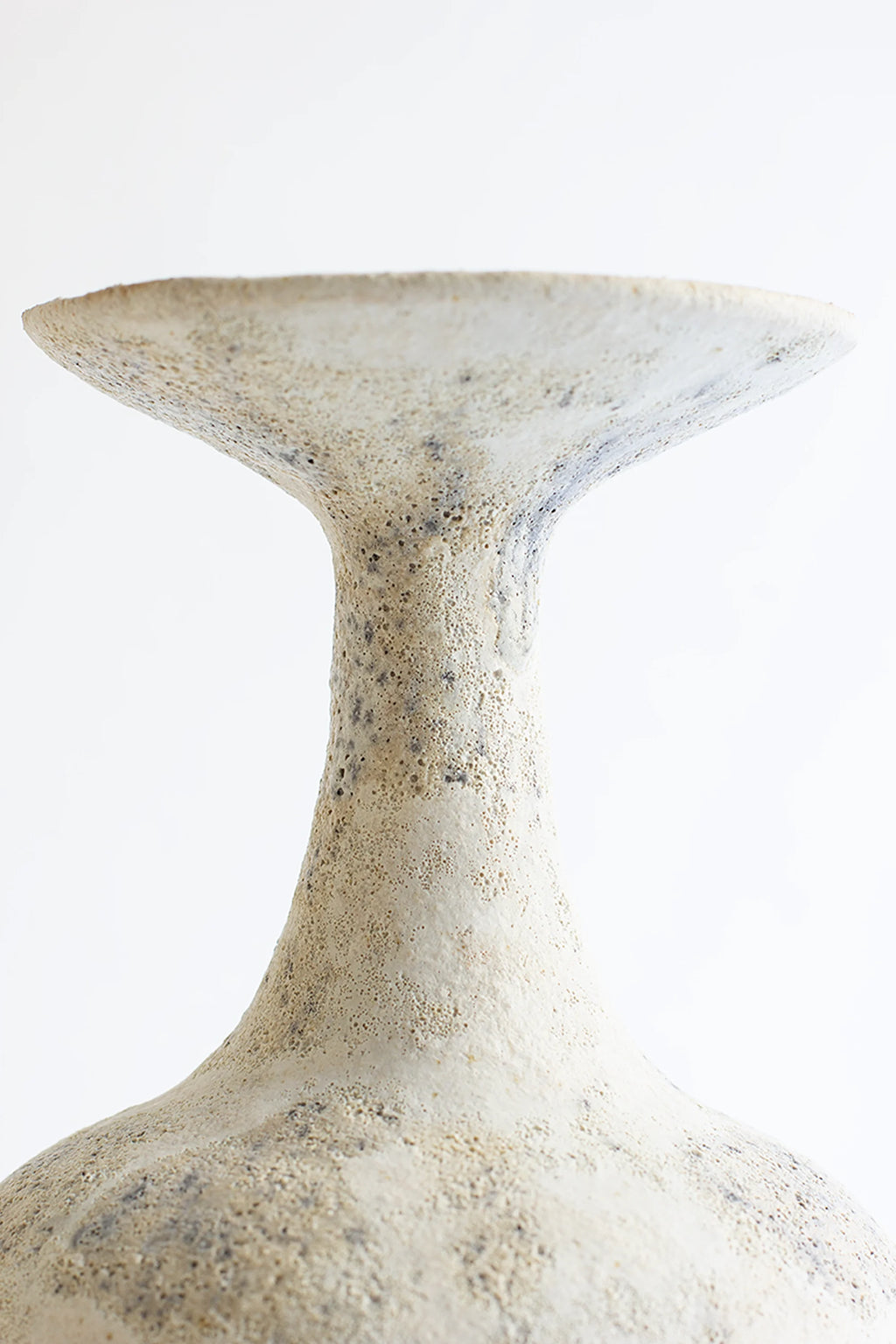 Canoa Lab Arq 002 Cárabo Vase, a handcrafted cream ceramic vase featuring a uniquely porous and textured surface with subtle dark grey specks, showcasing an organic sculptural shape with a wide, flat rim and elegant tapering neck. This wabi-sabi inspired stoneware vase is perfect for minimalist shelf styling, adding rustic elegance to living room decor or entryway consoles.