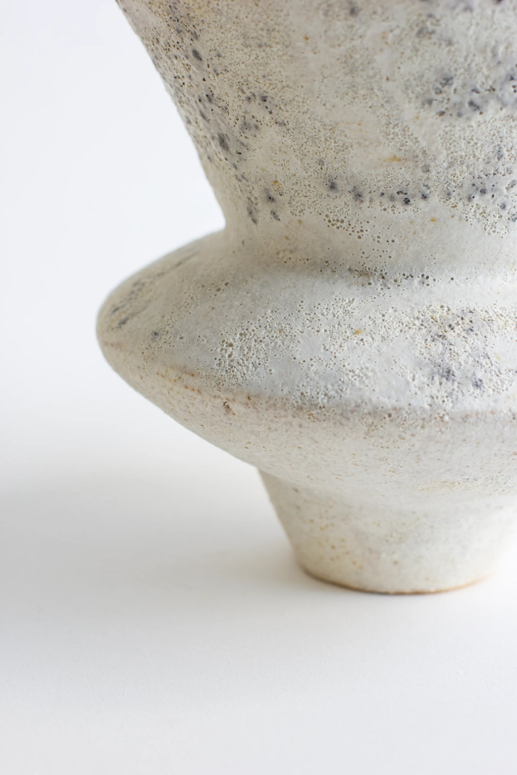 Canoa Lab Arq 010 Cárabo Vase, a modern ceramic design with a textured, off-white and gray speckled finish, featuring a distinctive rounded base and elegant, tapering form, on a white background.