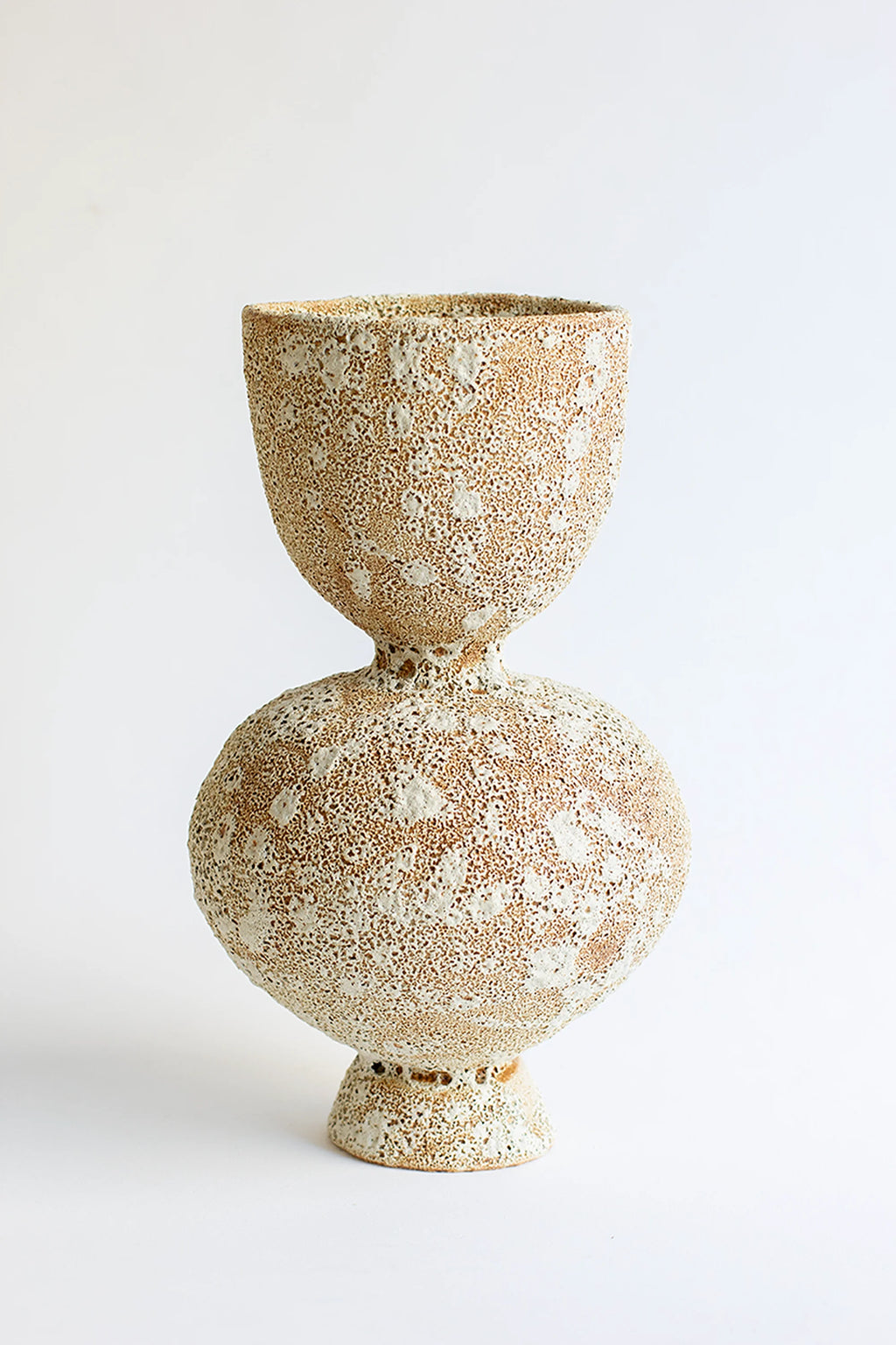 Canoa Lab Arq 013 Vase, a unique, hourglass-shaped ceramic vase with a distinctive textured surface. The vase features a warm, sandy beige base with raised, irregular white speckles, creating a tactile, modern aesthetic. Displayed on a clean white background.
