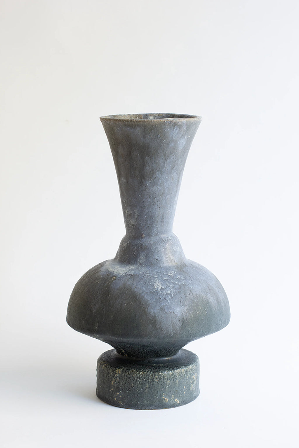 Canoa Lab Arq 014 Vase, a dark charcoal handcrafted stoneware vase with a raw, porous texture and a striking sculptural silhouette, featuring a bulbous body, narrow waist, and.