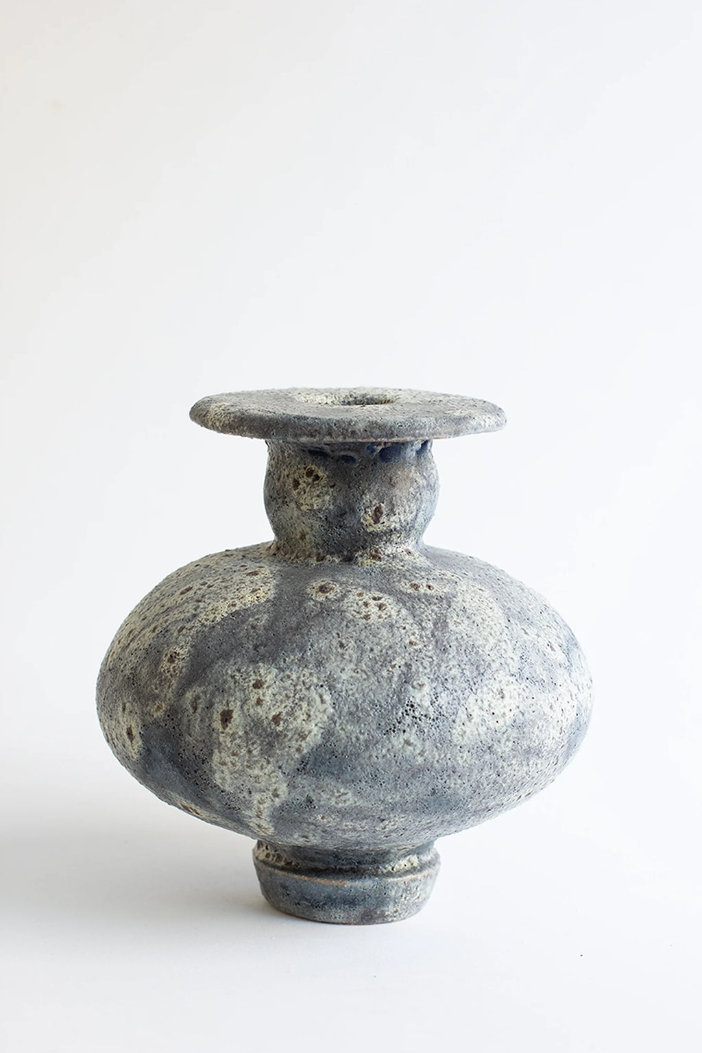 Canoa Lab Cálpide Gecko Vase, a unique, handcrafted ceramic vase with a bulbous body and a flat, wide rim. It features a textured, mottled gray and white glaze, resembling natural stone, displayed on a clean white background.