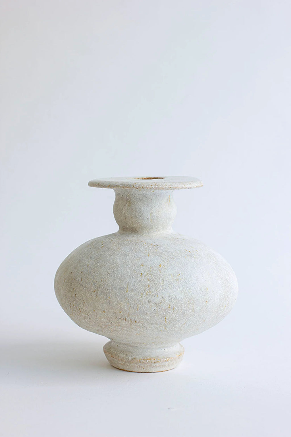 Canoa Lab Cálpide Blanco Hueso Vase, an elegant, handcrafted ceramic vase with a smooth, bulbous body and a flat, wide rim. It features a subtle, matte off-white bone-colored glaze, exuding minimalist sophistication, displayed on a white background.