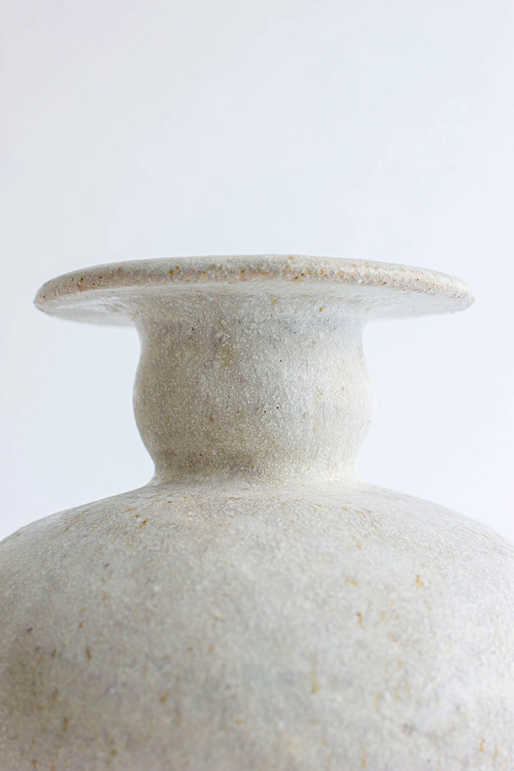 Canoa Lab Cálpide Blanco Hueso Vase, a detailed side view of the neck and rim, highlighting the artisanal, textured off-white ceramic. The unique, organic shape and subtle speckles create a premium, classic aesthetic, displayed on a white background.