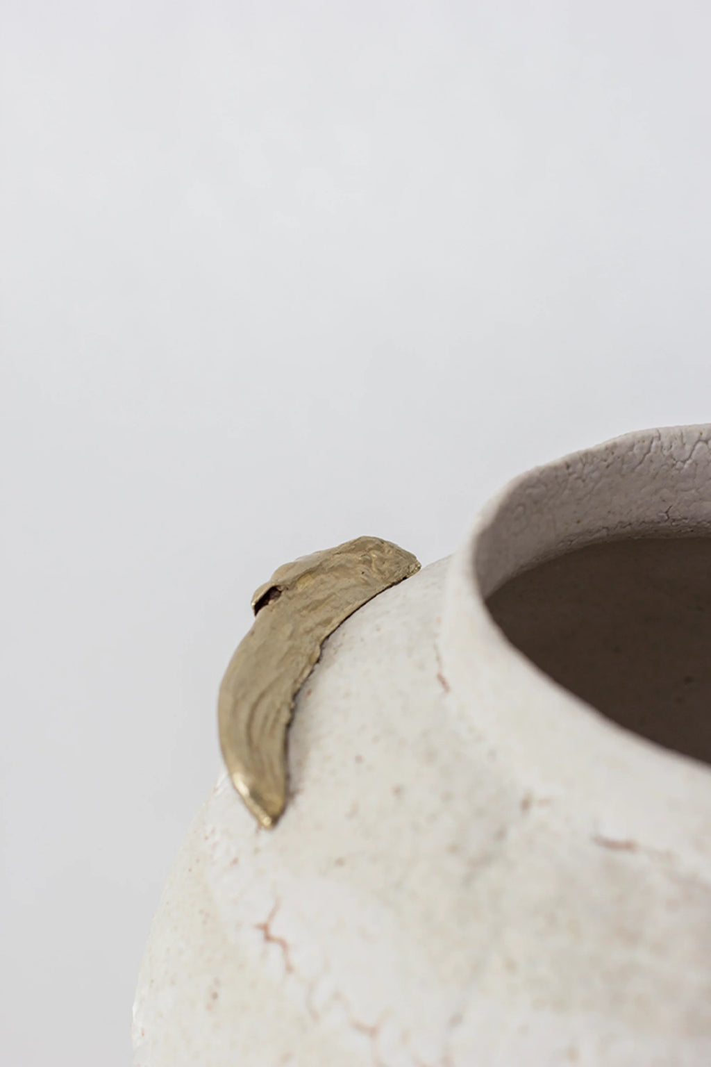 Canoa Lab Isolated n.10 Vase, a close-up of the vase's rim, showcasing one of the golden, leaf-like accents and the textured, off-white ceramic surface with subtle crackling, displayed on a white background.