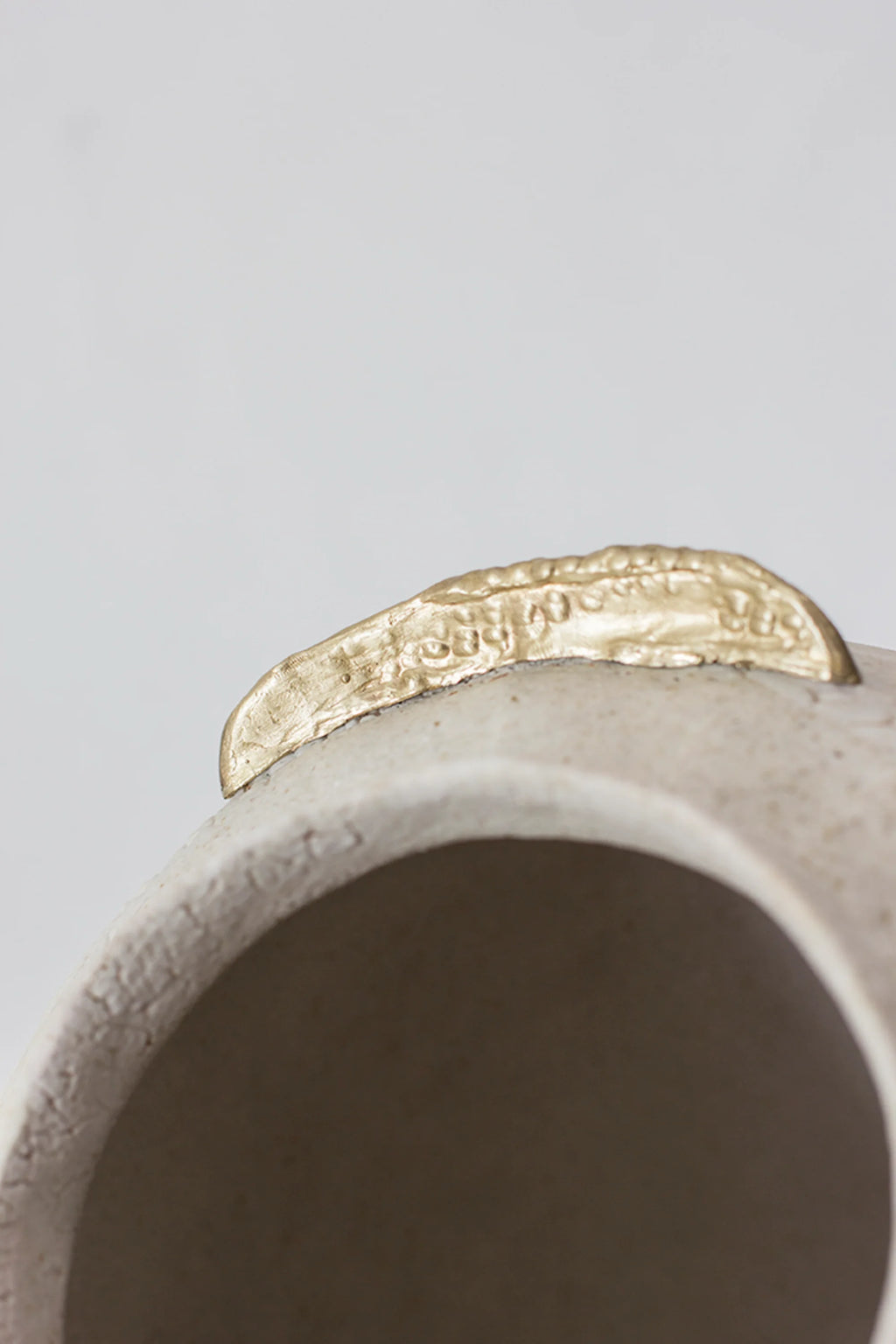 Canoa Lab Isolated n.10 Vase, an extreme close-up of one golden, leaf-like accent on the vase's rim, showing its textured, metallic finish and the subtle details of the off-white ceramic, displayed on a white background.