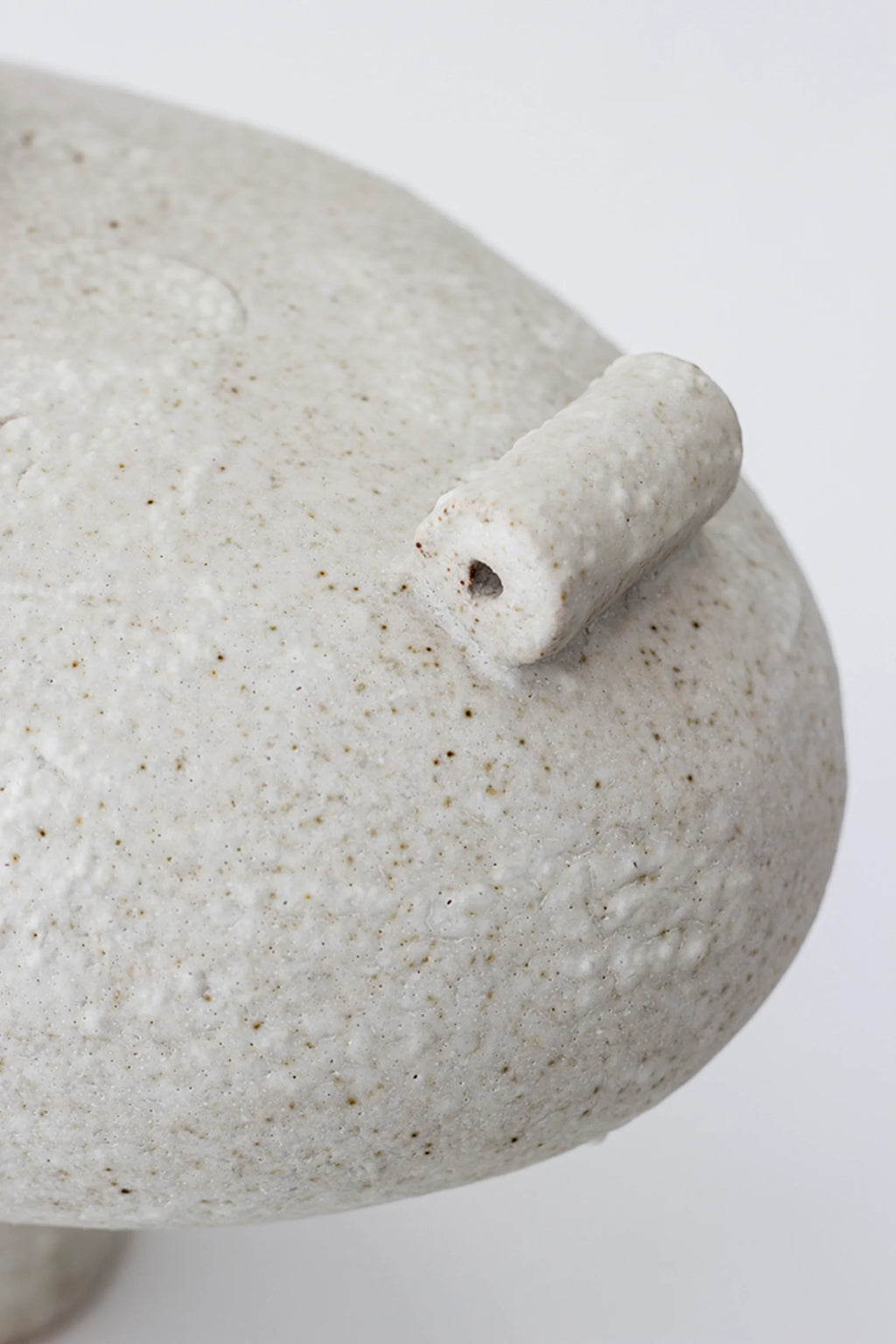 Canoa Lab Isolated n.13 Vase, a detailed close-up of the textured, off-white ceramic body with a small, cylindrical handle protruding, showcasing the rustic, granular finish on a white background.
