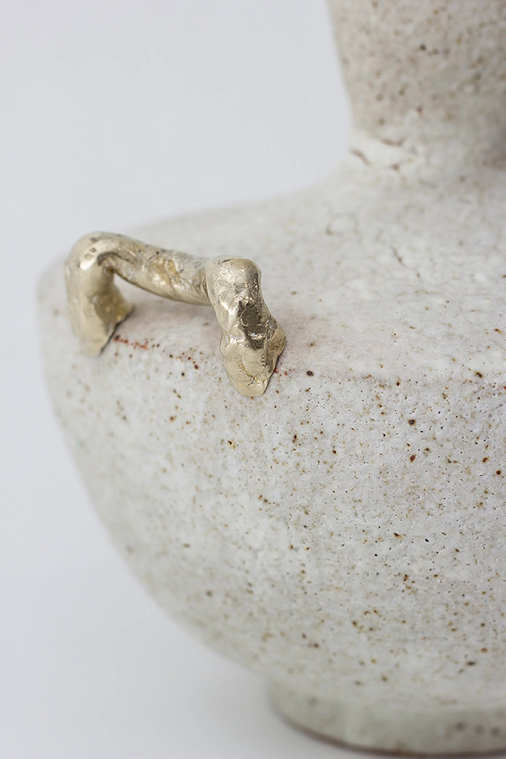 Canoa Lab Isolated n.15 Vase, a unique, handcrafted ceramic vase in a speckled off-white finish, featuring a distinctive gold-toned, organic-shaped handle on its textured surface, displayed on a clean white background.