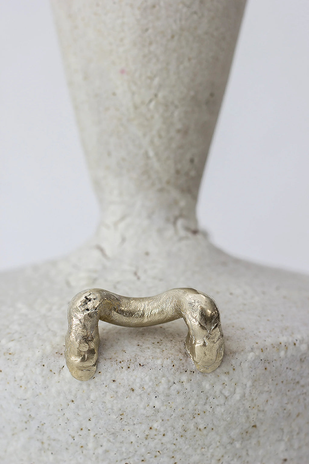 Canoa Lab Isolated n.15 Vase, a close-up of the elegant, textured off-white ceramic vase, showcasing a prominent gold-toned, abstract, bridge-like handle on its speckled surface, presented on a minimalist white background.