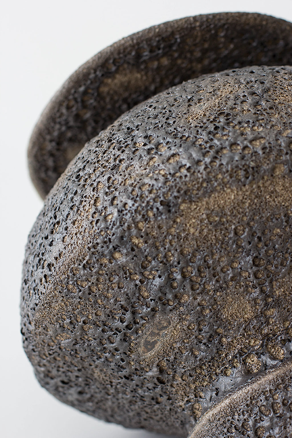 Canoa Lab Isolated n.18 Vase, a handcrafted artisanal stoneware vase featuring a dramatic dark charcoal finish with a highly textured, porous volcanic surface and subtle bronze undertones. Its organic, sculptural form and Brutalist-inspired texture make it a striking decorative object for minimalist living rooms, organic modern shelf styling, or contemporary entryways.