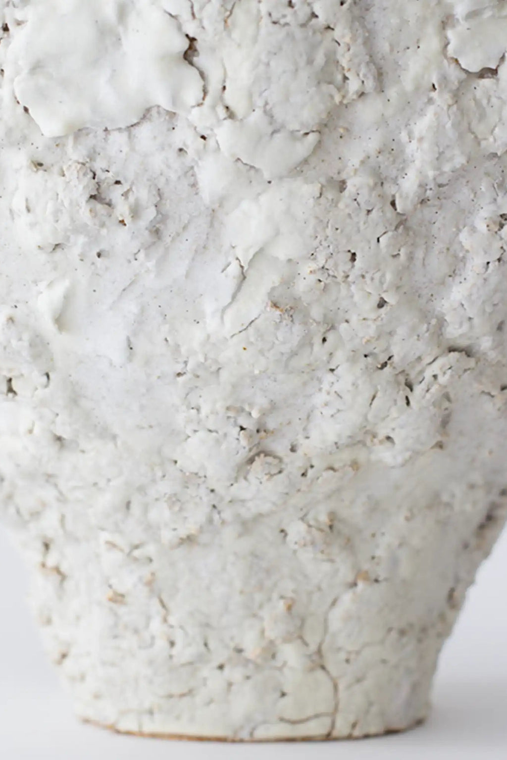 Canoa Lab Isolated n.21 Vase, a handcrafted ceramic vase in an off-white natural tone, featuring a heavily textured and porous volcanic surface with subtle grey and warm speckles. Its organic, craggy finish and sculptural form create a unique stoneware piece with a wabi-sabi aesthetic. Ideal for organic modern shelf styling or as a rustic accent in contemporary living rooms and bedrooms.