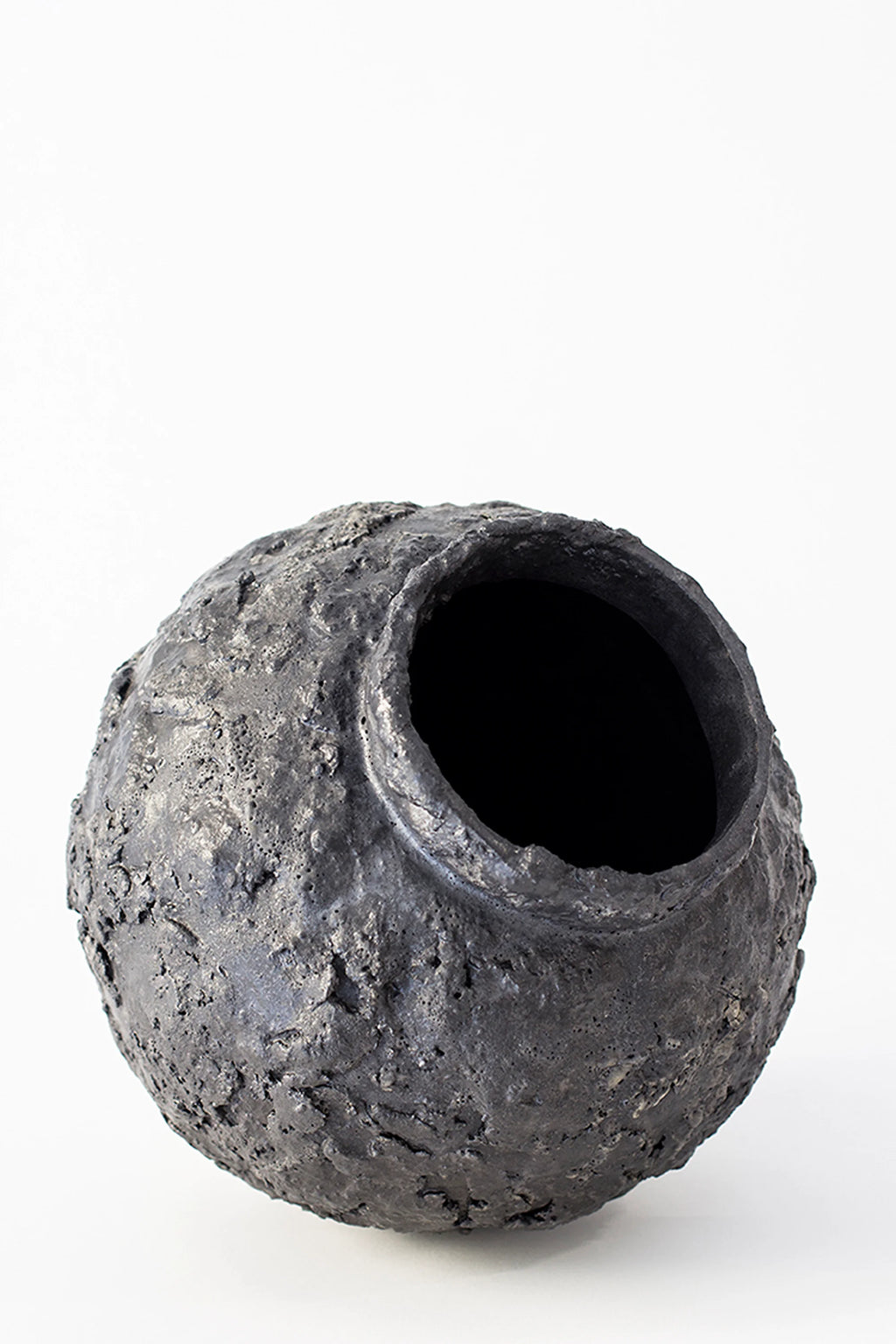 Canoa Lab Isolated n.22 Vase, a side view of the dark gray, spherical ceramic vase, revealing its unique, textured surface and the wide, dark opening, on a white background.