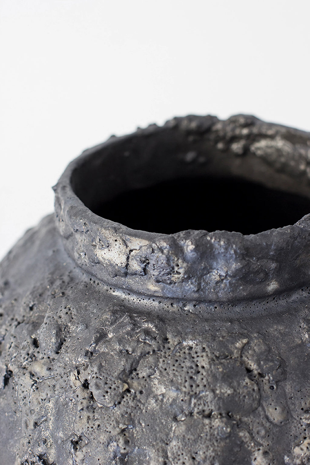 Canoa Lab Isolated n.22 Vase, a close-up of the opening and upper portion of the dark gray, spherical ceramic vase, emphasizing its raw, textured finish and craftsmanship.