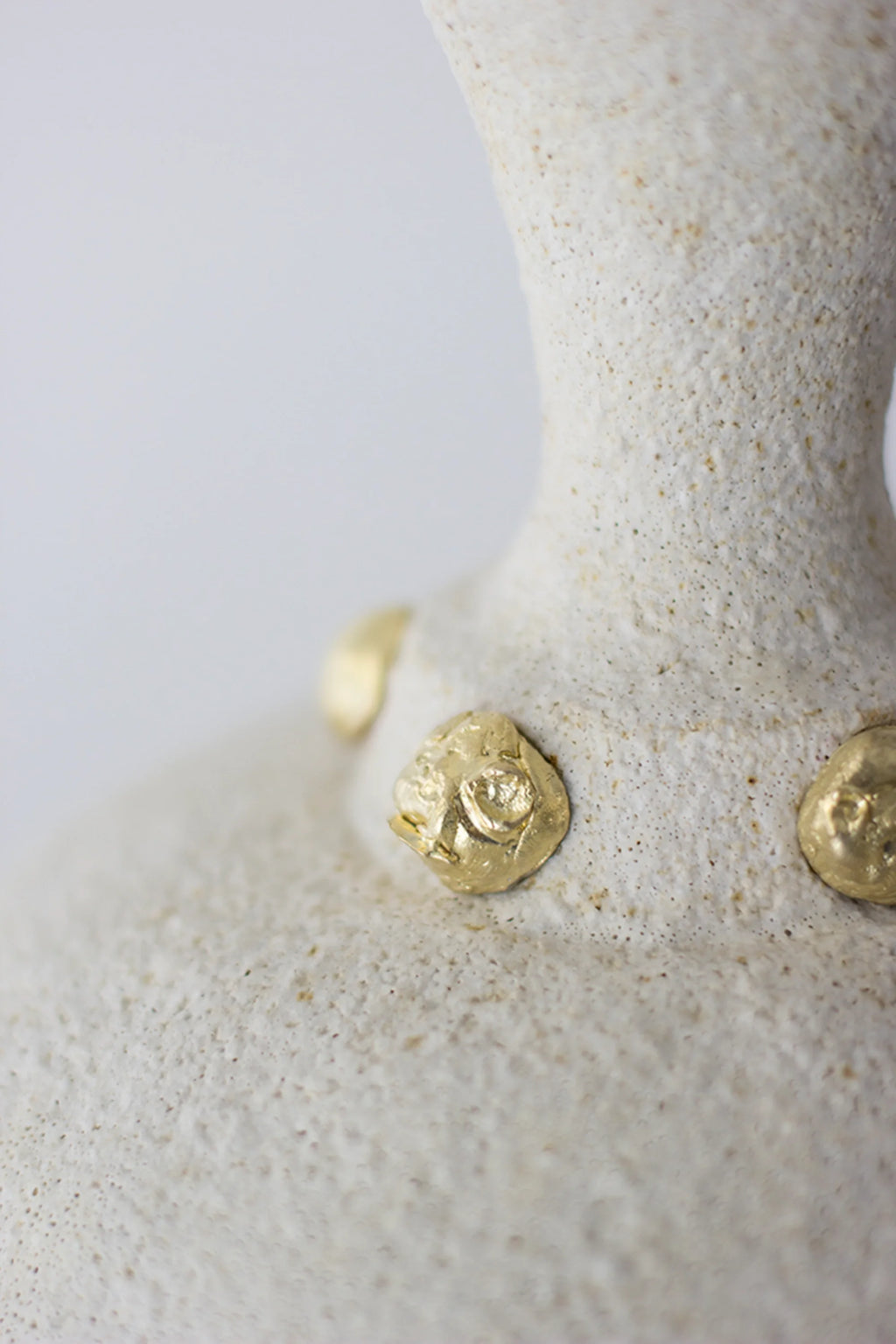 Canoa Lab Isolated n.24 Vase, a close-up view highlighting the intricate golden embellishments and the rough, tactile texture of the off-white ceramic material, presented on a white background.