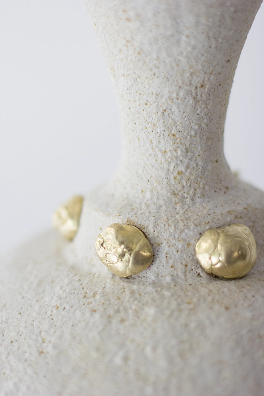 Canoa Lab Isolated n.24 Vase, a detailed shot emphasizing the organic, irregular golden accents against the coarse, off-white ceramic surface, showcasing its artisanal quality on a white background.