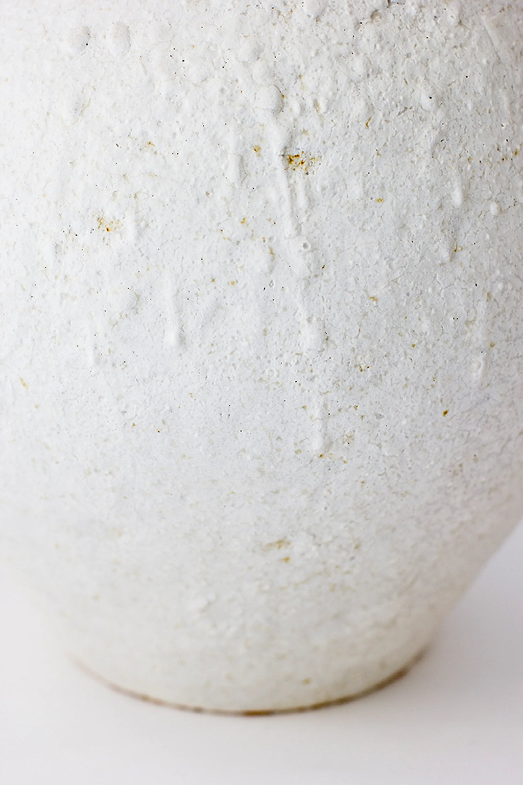 Canoa Lab Isolated n.26 Vase, a detailed close-up of the lower, rounded section of the elegant vase, highlighting its rough, speckled off-white ceramic texture with subtle brown flecks, on a white background.