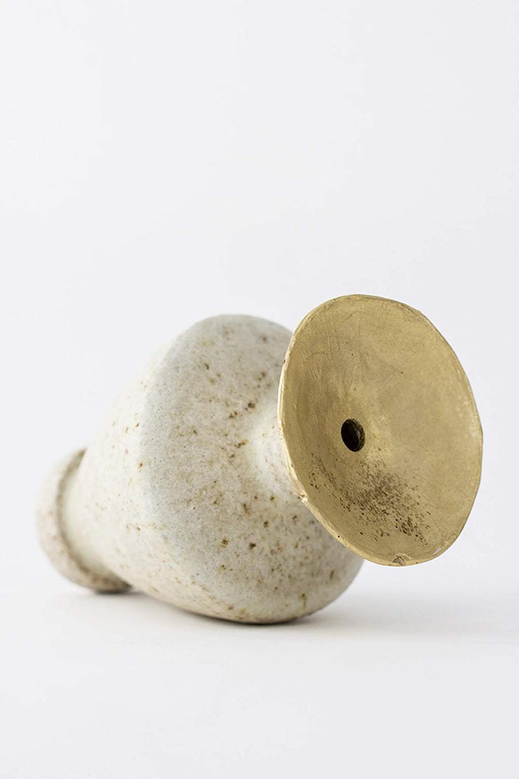 Canoa Lab Isolated n.6 Vase, positioned on its side, revealing the full conical shape of the speckled off-white ceramic body and the elegant brass top with its central hole.