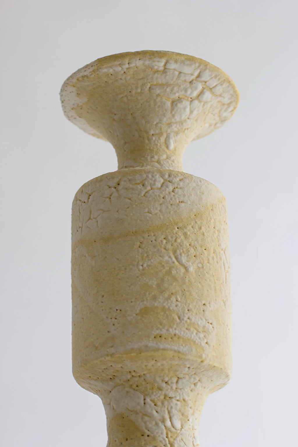 Canoa Lab Isolated n.30 Vase, a handcrafted stoneware ceramic vase in warm cream and sandy yellow tones, featuring a highly textured, porous, and crackled volcanic finish. Its unique sculptural silhouette with a flared top, narrow neck, and cylindrical body embodies an organic modern or brutalist aesthetic. Perfect as a statement piece for contemporary shelf styling, minimalist living rooms, or wabi-sabi inspired interiors.
