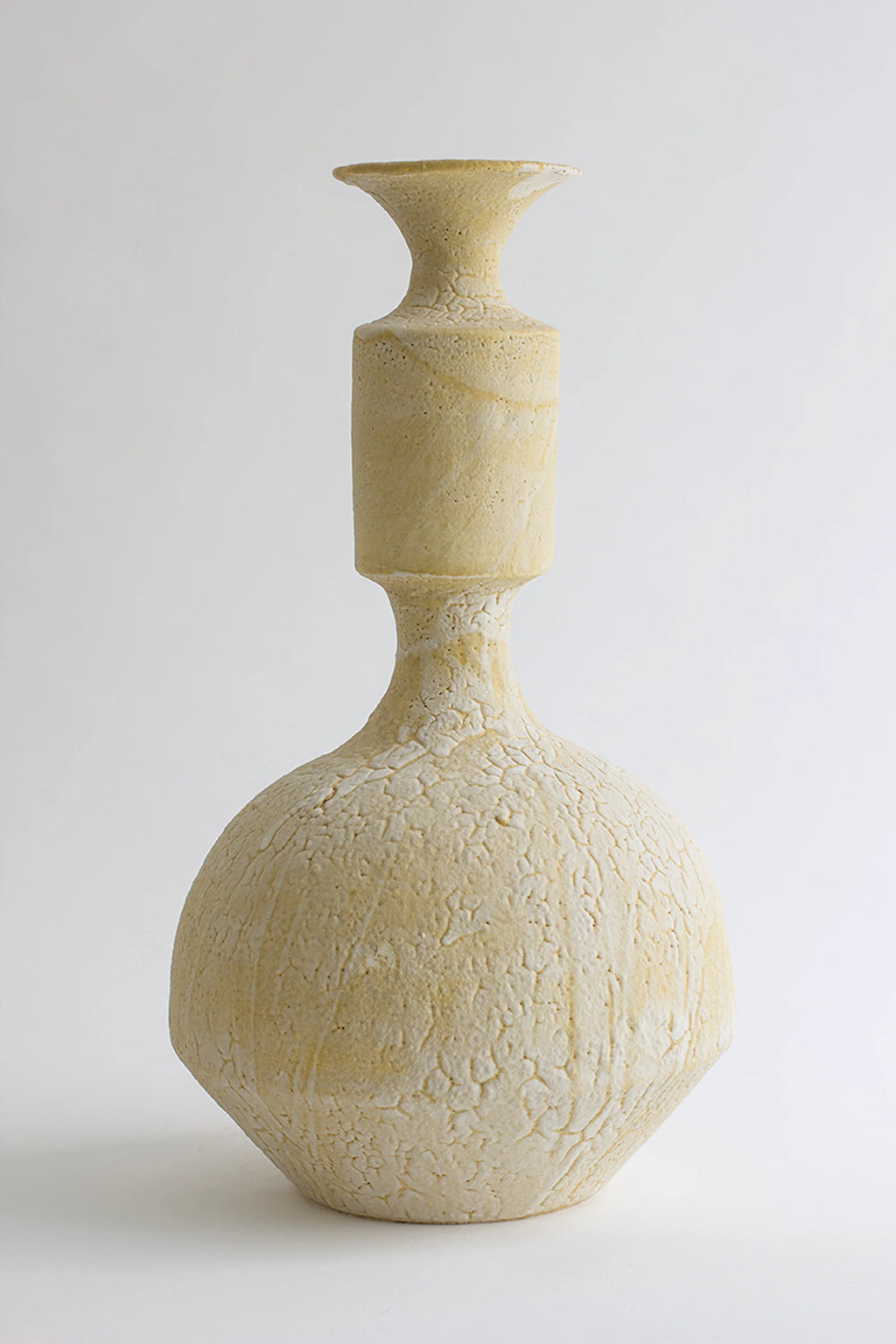 Canoa Lab Isolated n.30 Vase, a sculptural cream-colored handcrafted ceramic vase featuring a unique bulbous base, a narrow neck, and a cylindrical body with a flared top. Its heavily textured, porous volcanic finish in warm off-white and sandy tones evokes an organic modern or brutalist aesthetic, perfect for minimalist shelf styling or contemporary living room decor.