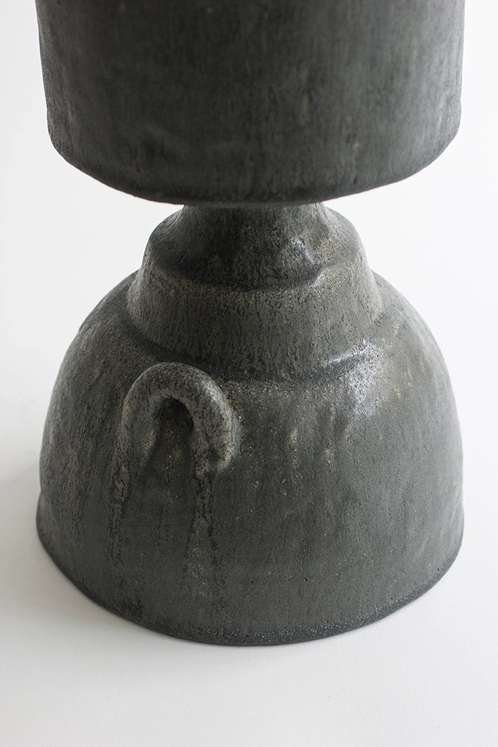 Canoa Lab Isolated n.32 Vase, a detailed close-up of the robust, bell-shaped base of the dark gray ceramic vase, showcasing its textured, matte surface and the subtle curve of its integrated handles, on a white background.