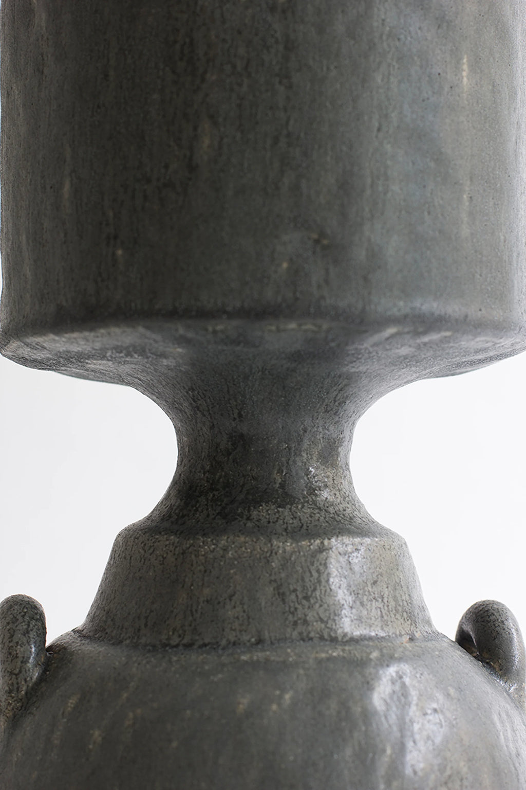 Canoa Lab Isolated n.32 Vase, a close-up of the elegant dark gray ceramic vase, focusing on the intricate connection between its cylindrical body and the bell-shaped base, highlighting the textured, matte finish, on a white background.