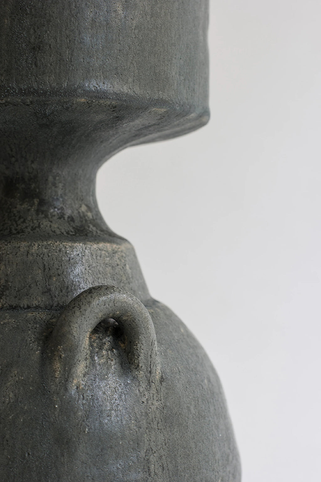Canoa Lab Isolated n.32 Vase, a close-up of the elegant dark gray ceramic vase, highlighting the textured, matte finish of its bell-shaped base and one of its small, integrated loop handles, against a white background.