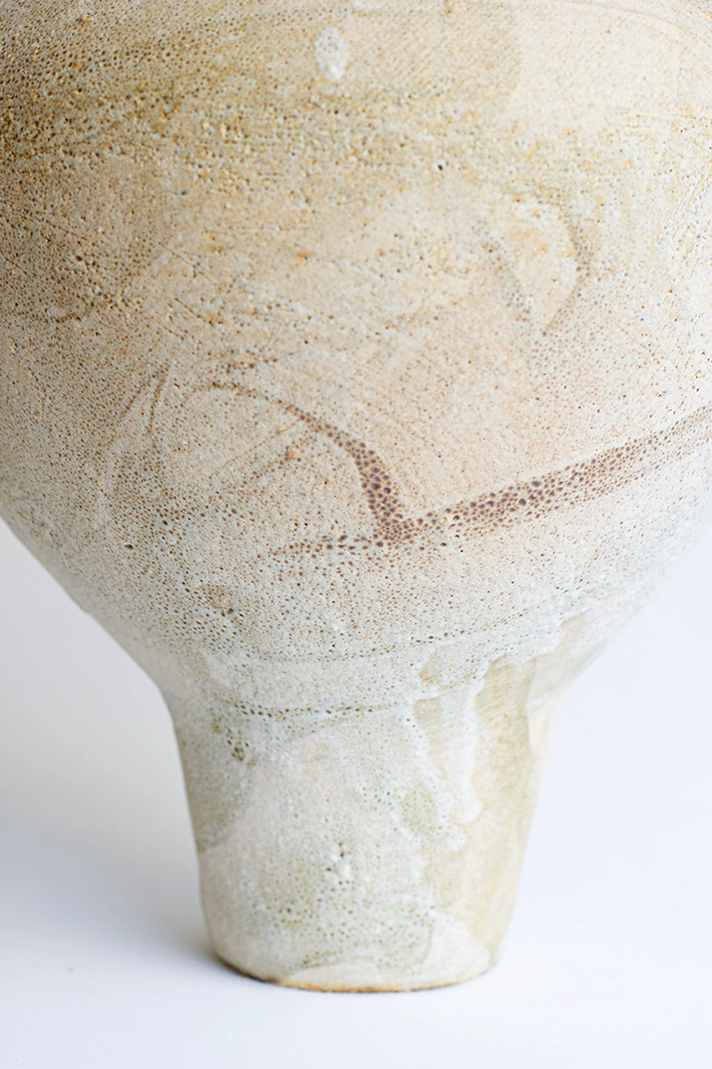 Canoa Lab Isolated n.35 Vase, a detailed close-up of the vase's lower body, highlighting its smooth, off-white ceramic texture with subtle natural markings and a gently curved form, presented on a white background.