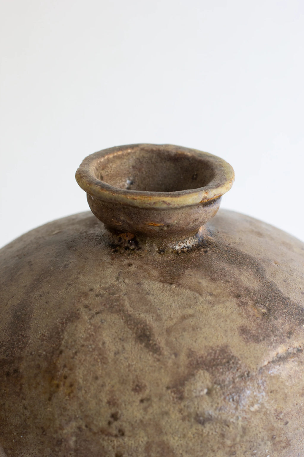 Canoa Lab Lebes Búfalo Vase, a close-up of the top opening, showcasing the rustic, earthy brown and green glazed ceramic with a textured, weathered finish and a small, rounded rim.