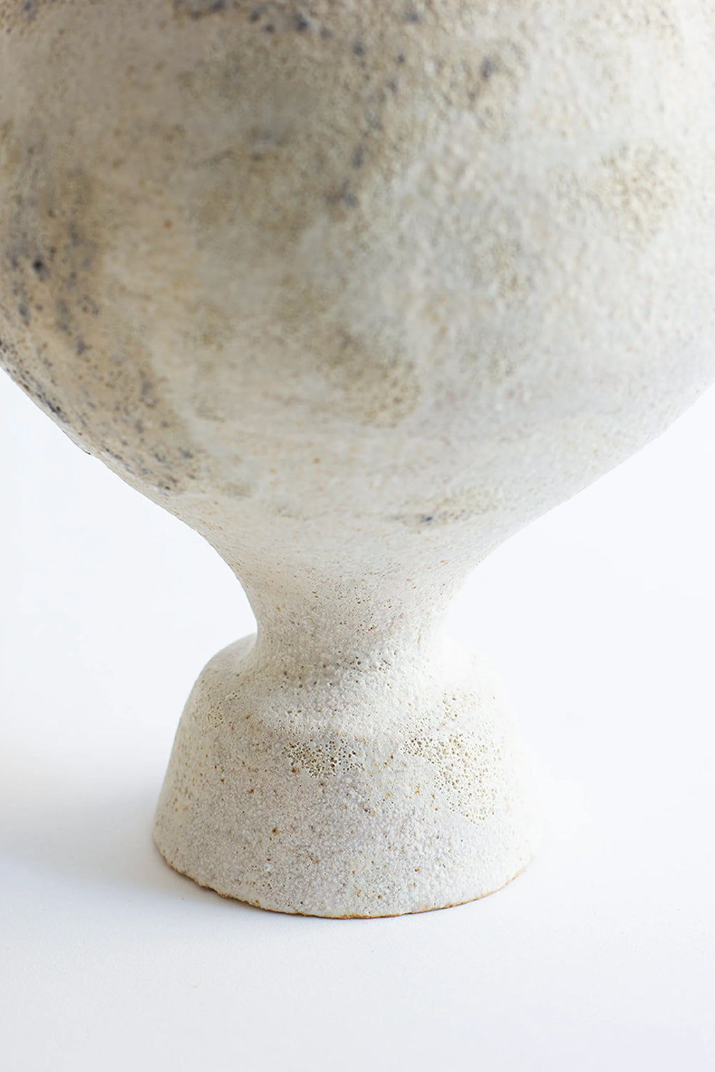 Canoa Lab Lekytho Cárabo Vase, a close-up of the sturdy, textured base and lower body of the artisanal ceramic vase, revealing the granular off-white finish and subtle organic variations, displayed on a white background.