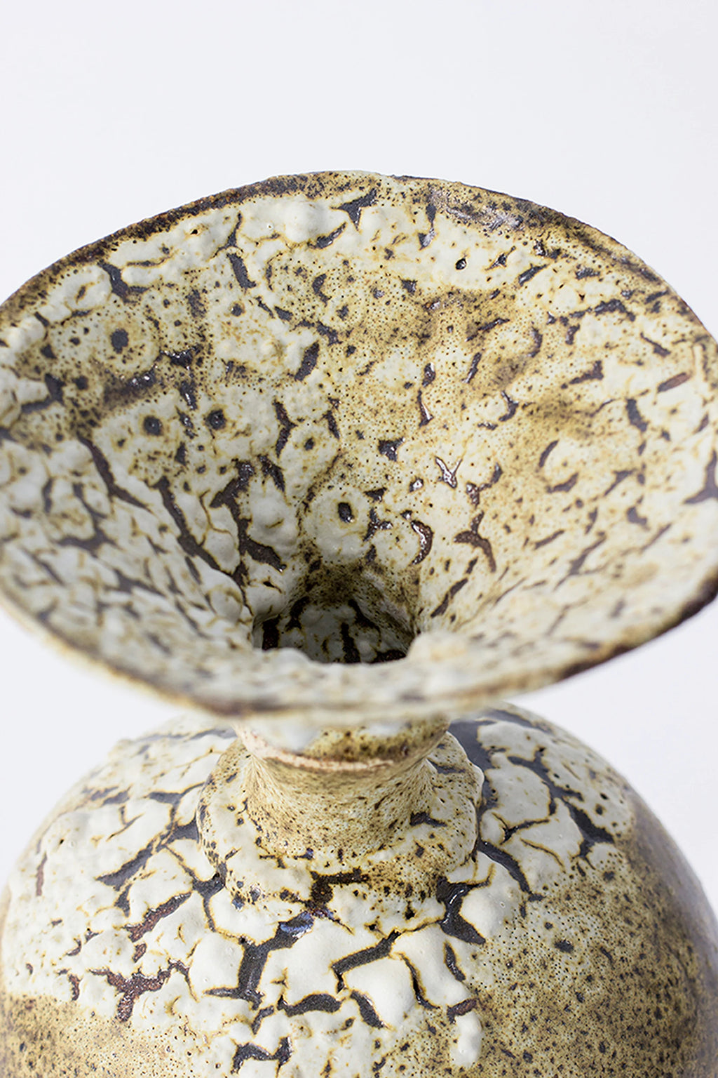 Canoa Lab Ánfora Limonita Vase, an intricate top-down view into the vase's flared opening, emphasizing the unique crackled texture and earthy limonita yellow and white tones, on a white background.