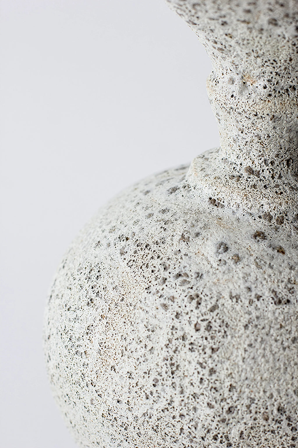 Canoa Lab Ánfora Vase, a side view close-up of the vase's curved body and neck, emphasizing the organic, textured light gray ceramic surface with dark, speckled details, presented on a white background.