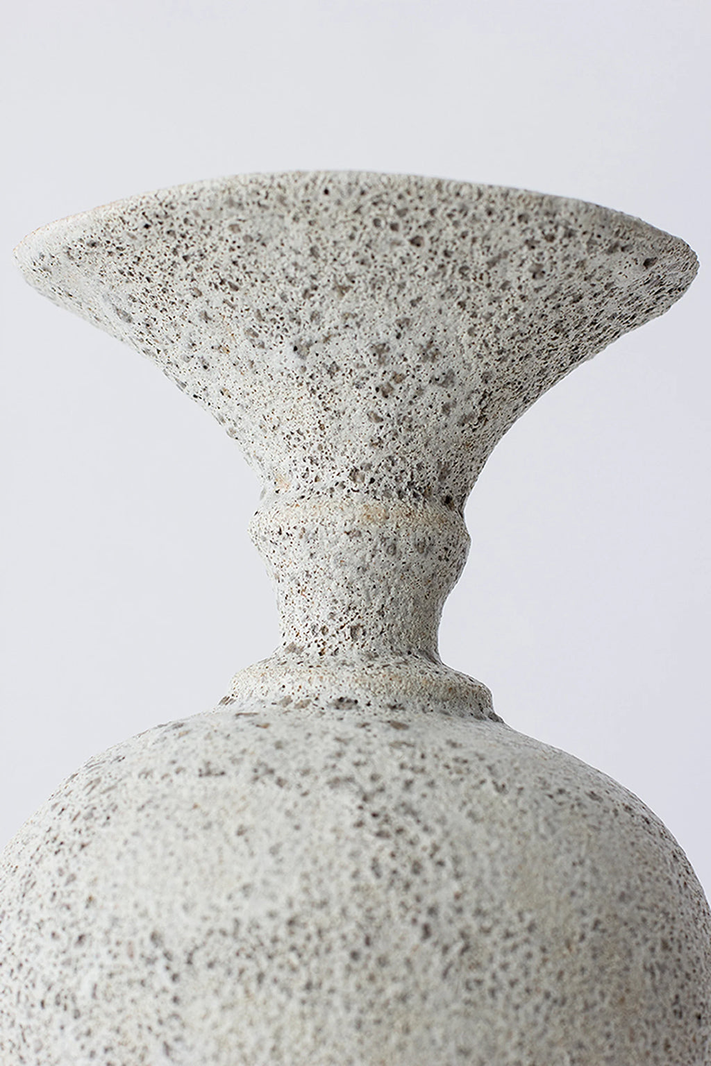 Canoa Lab Ánfora Vase, a detailed view of the vase's neck and upper body, highlighting the rustic, textured light gray ceramic finish with dark, speckled patterns, against a bright white background.