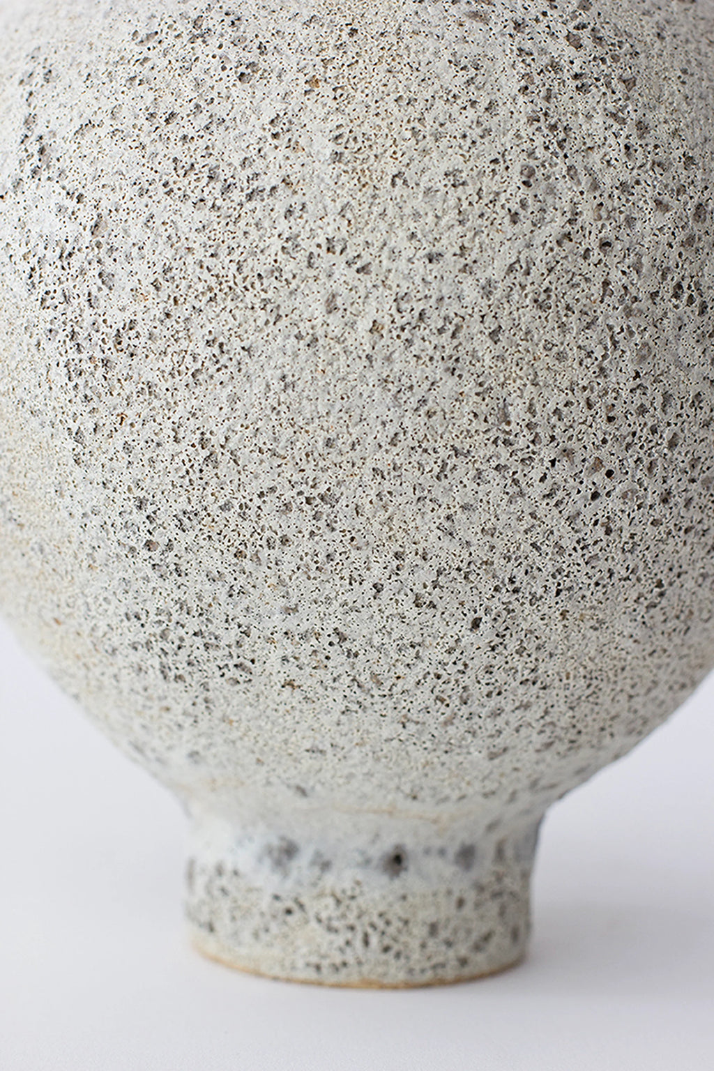 Canoa Lab Ánfora Vase, a close-up of the vase's rounded base, revealing the intricate, porous texture of the light gray ceramic with dark speckles, showcasing its artisanal craftsmanship on a white background.