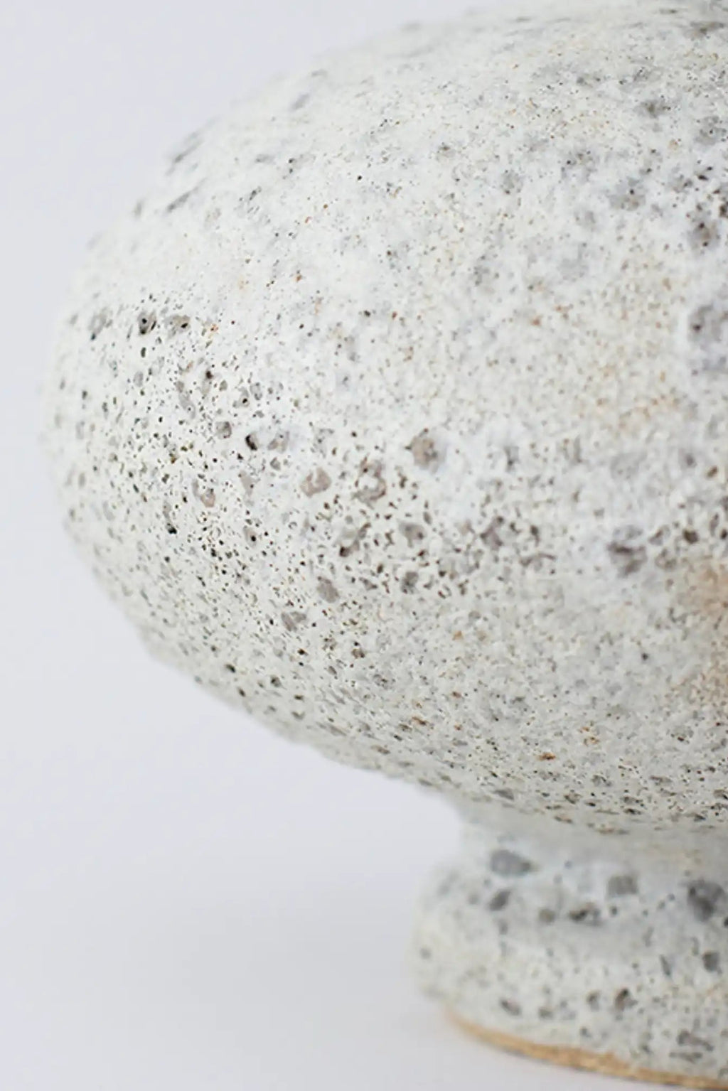 Canoa Lab Cálpide Vase, a handcrafted ceramic vase with a distinctive porous volcanic texture and an organic, bulbous silhouette, finished in a raw, speckled off-white and grey glaze.