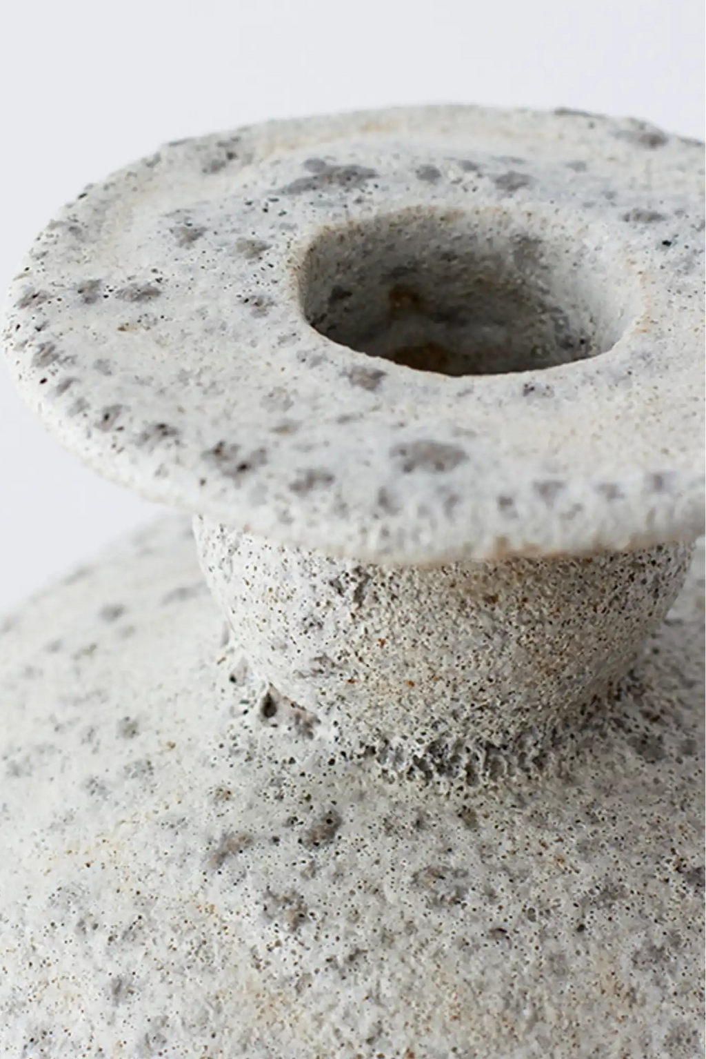Canoa Lab Cálpide Vase, a cream-colored handcrafted ceramic vase featuring a distinctive porous volcanic texture in warm off-white and speckled grey tones, with a subtly flared rim and an organic, rustic silhouette. This artisanal stoneware piece is ideal for minimalist shelf styling, adding an organic modern accent to living rooms, or enhancing japandi and wabi-sabi interiors.
