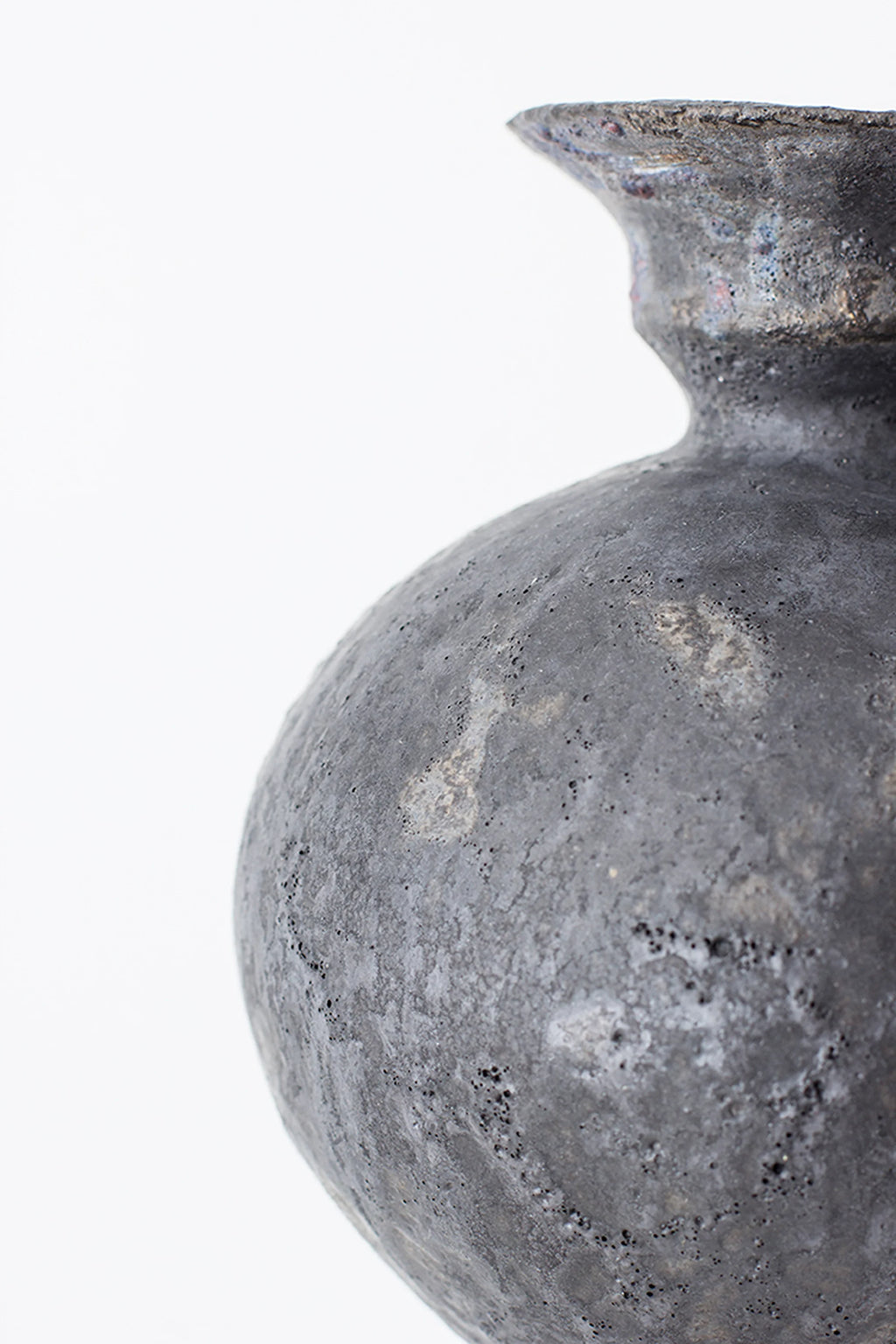 Canoa Lab Lekytho Vase, a handcrafted dark grey ceramic vase with a unique volcanic texture and porous, pitted finish, featuring subtle reddish-brown and metallic undertones.