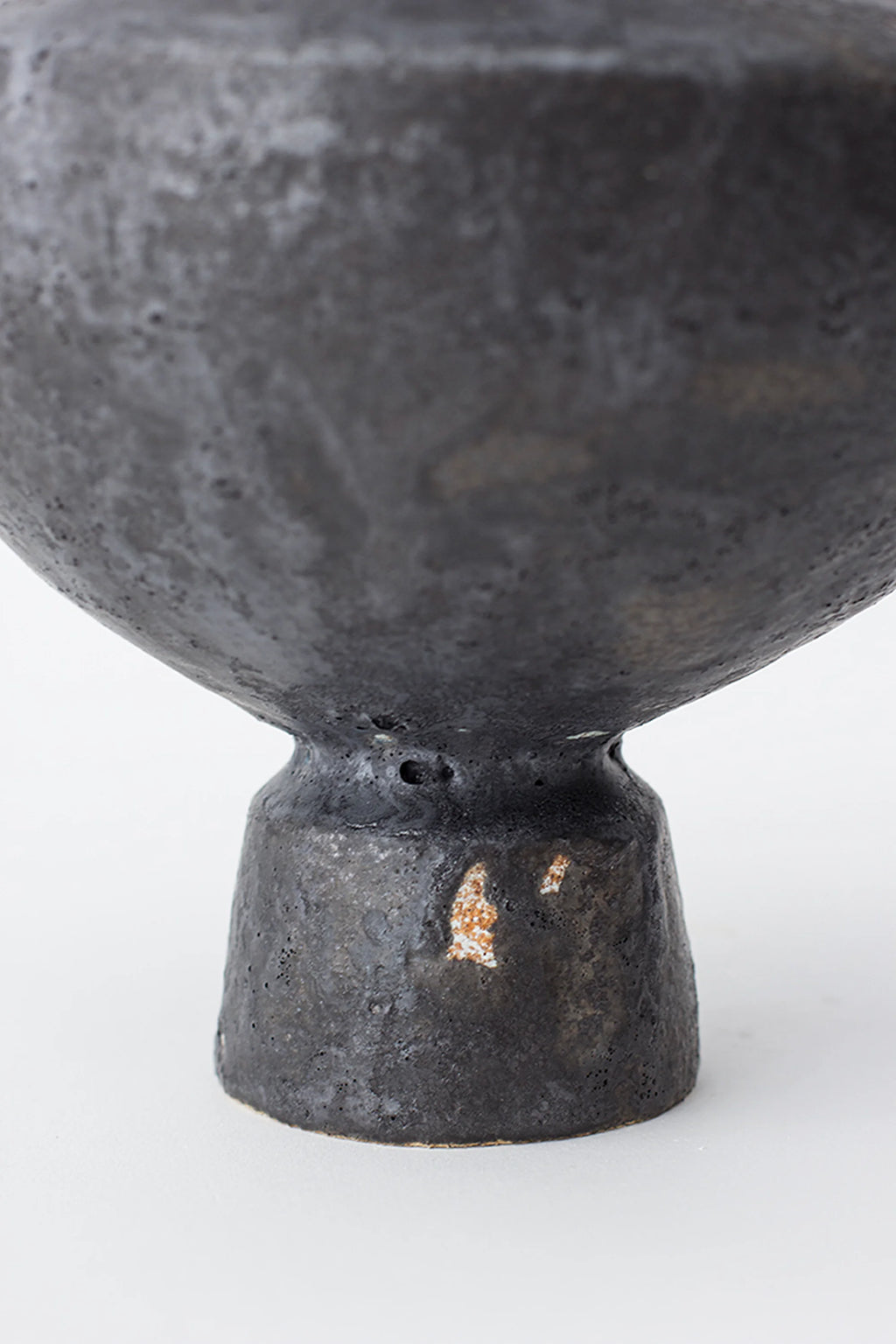Canoa Lab Lutróforo Vase, a detailed shot of the vase's base, showcasing its sturdy, handcrafted dark gray ceramic material with subtle brown undertones, on a white background.