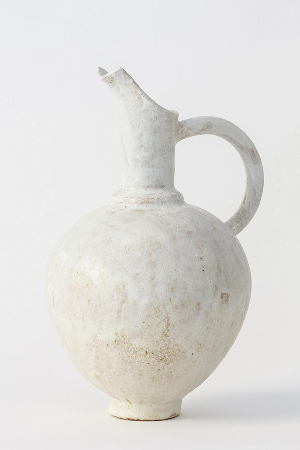Canoa Lab Oinochoe Perla Pitcher, a handcrafted off-white ceramic vase with a rustic, porous texture and natural earthy speckles, featuring a bulbous body, elegant handle, and distinct pouring spout. This artisanal stoneware piece offers an organic modern aesthetic, perfect as a decorative pitcher or minimalist vase for shelf styling in wabi-sabi or Mediterranean-inspired interiors.