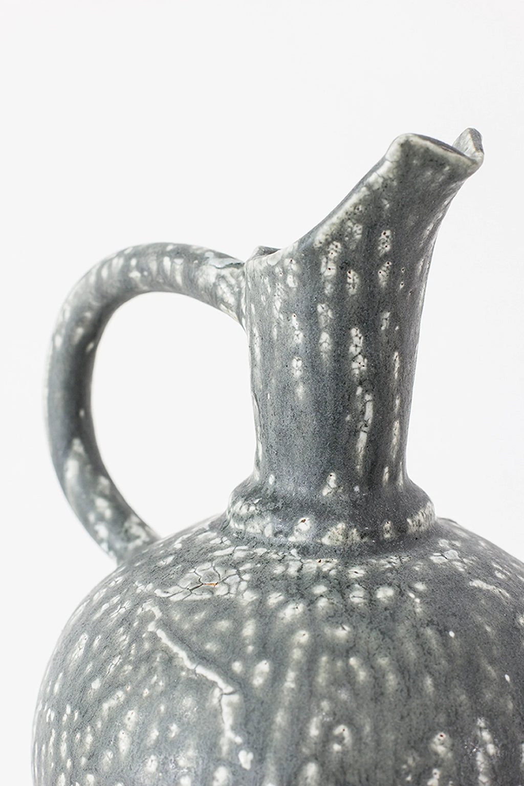 Canoa Lab Oinochoe Perla Negra Pitcher, a close-up of the pitcher's handle and spout, showcasing the intricate speckled white glaze on dark gray ceramic, highlighting its artisanal texture and design.