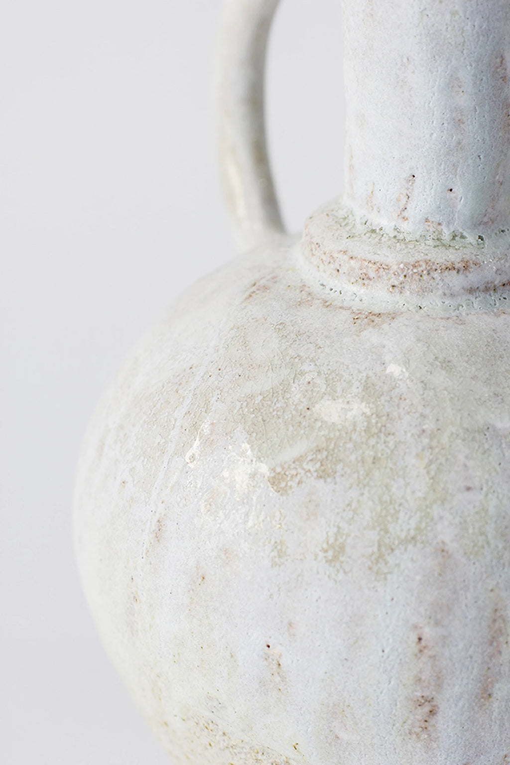 Canoa Lab Oinochoe Perla Pitcher, a handcrafted ceramic vase with a unique textured porous finish, showcasing an off-white and cream palette with subtle pale green and warm sand undertones. This artisanal stoneware piece features a rustic, organic surface and a classic Oinochoe pitcher silhouette.