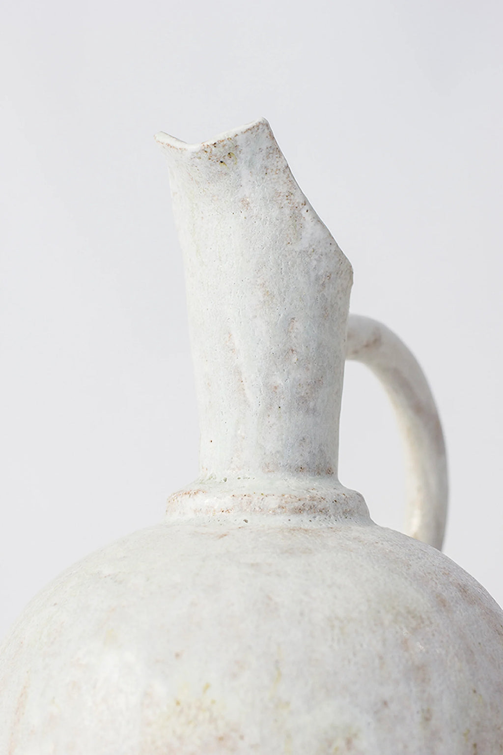 Canoa Lab Oinochoe Perla Pitcher, a close-up of the elegant, handcrafted ceramic pitcher's spout and neck, featuring a rustic, textured off-white glaze with subtle brown undertones, displayed on a clean white background.