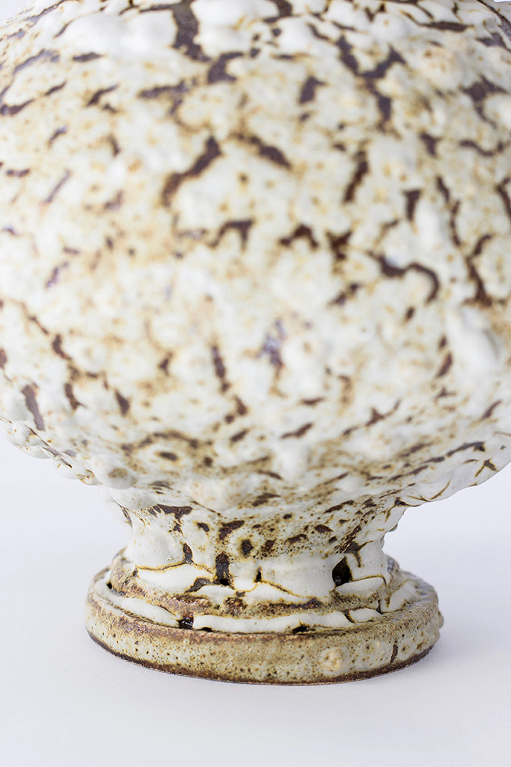 Canoa Lab Stamnos Limonita Vase, a detailed view of the vase's base and lower body, showcasing the rich, crackled white and brown glaze. The textured ceramic material and handcrafted details are prominent, displayed on a white background.
