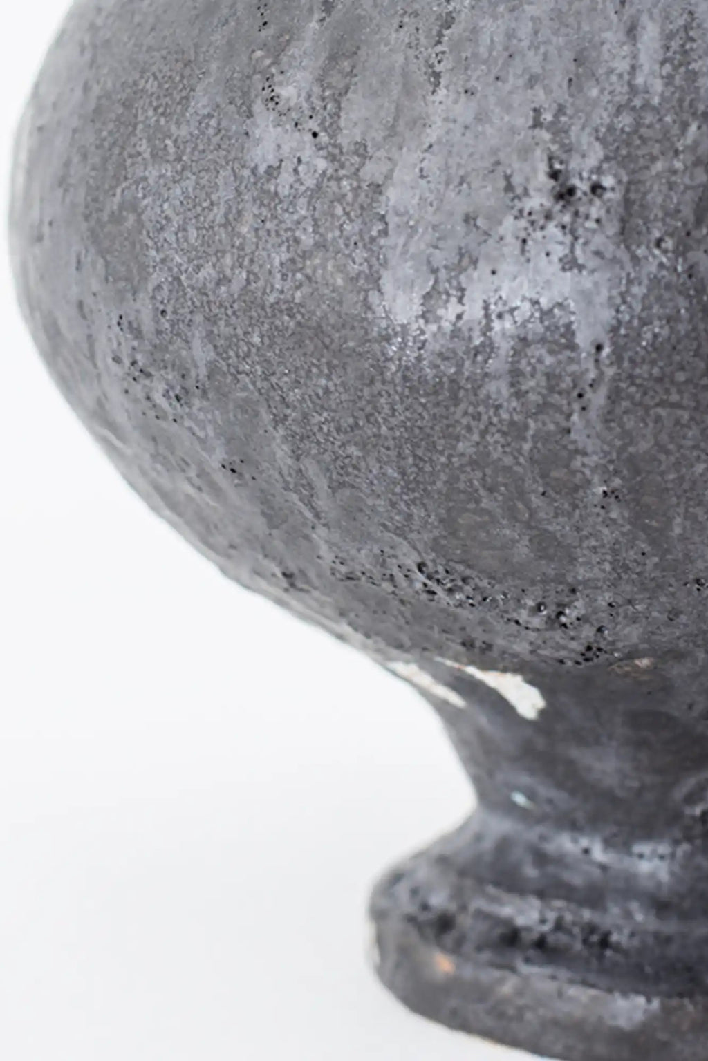 Canoa Lab Stamnos Vase, a dark grey handcrafted ceramic vase with a highly textured, porous, and volcanic-like finish, featuring a rounded body and fluted pedestal base. This brutalist-inspired stoneware piece adds organic modern style to minimalist shelf styling or contemporary living room decor.