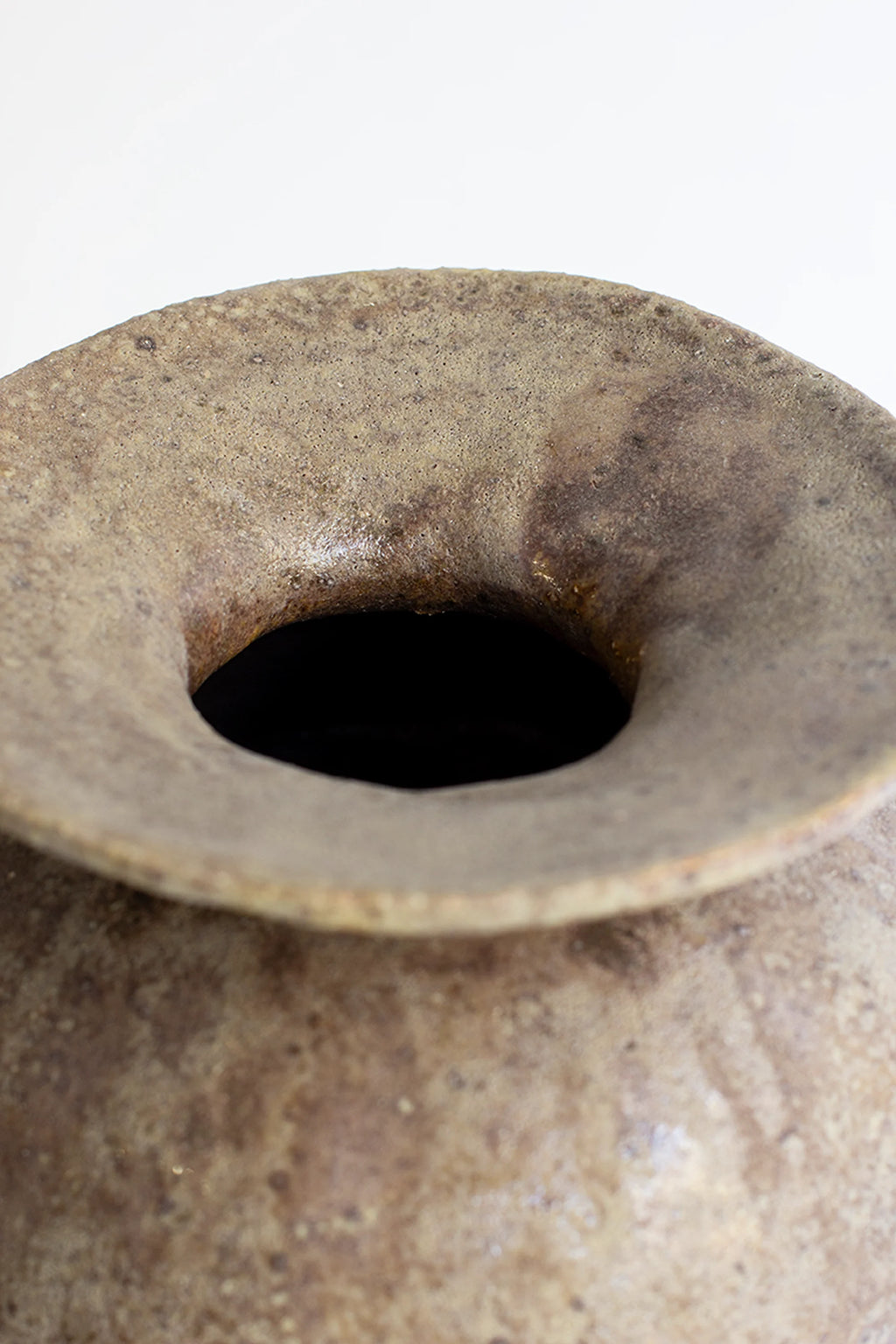 Canoa Lab Psycter Búfalo Vase, an overhead close-up shot of the vase's wide, flared opening, showcasing the raw, textured rim and the deep, dark interior of the earthy brown and green ceramic piece, on a white background.