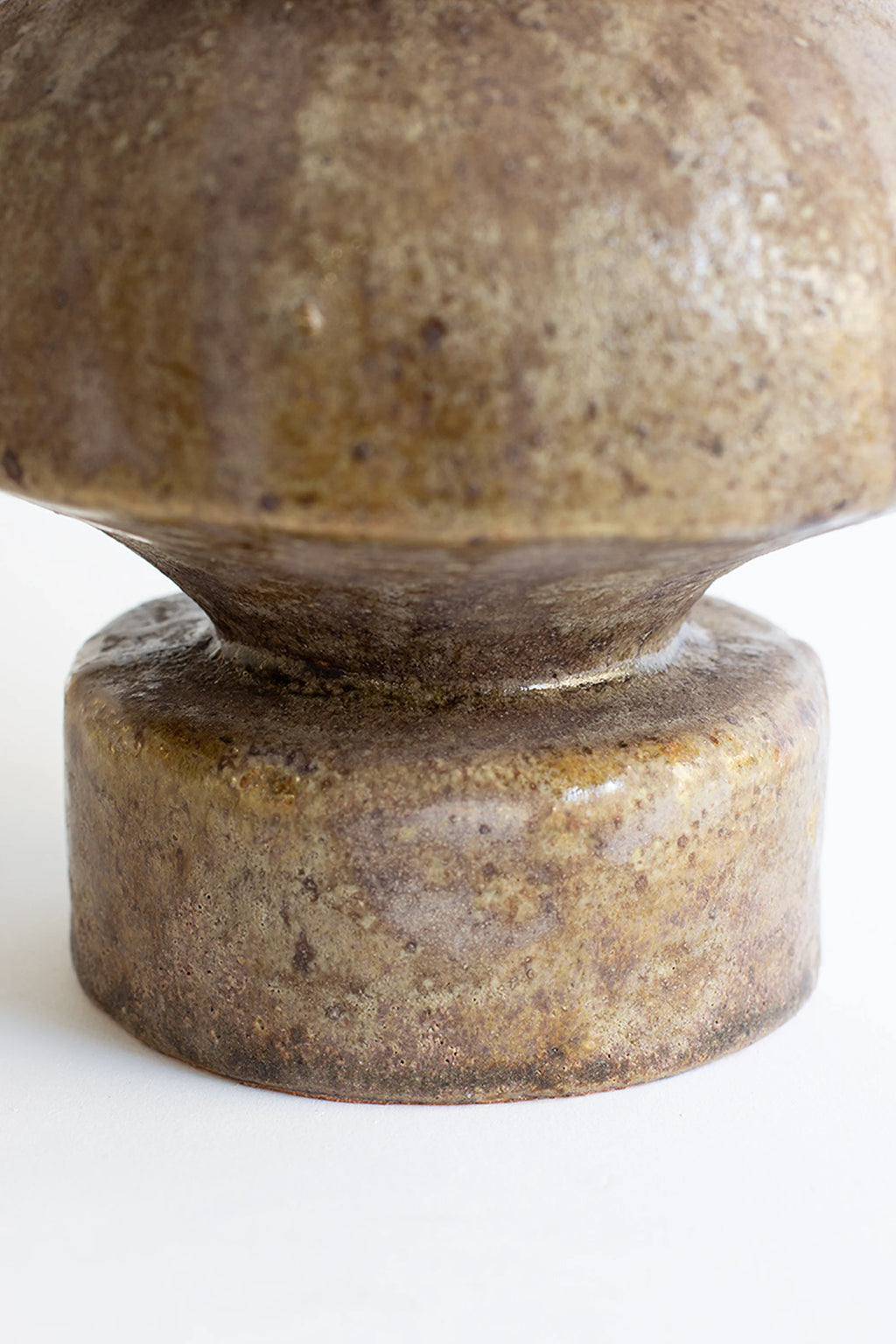 Canoa Lab Psycter Búfalo Vase, a close-up view of the sturdy base and lower body of the artisanal ceramic vase, revealing the rough, earthy texture and varied brown and green tones of its unique glaze, on a white background.