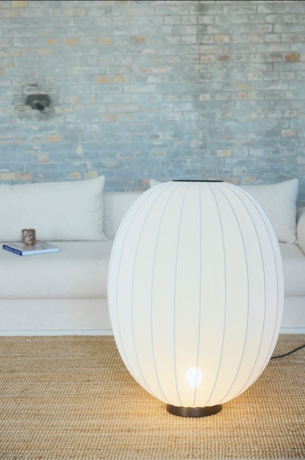 Made by Hand Knit-Wit Ø65 Floor Lamp, a large spherical modern floor lamp featuring a translucent white knitted textile shade with a distinct ribbed texture and a sleek dark metal base. This contemporary Scandinavian floor lamp provides warm ambient lighting for living rooms, bedrooms, or cozy minimalist reading nooks.