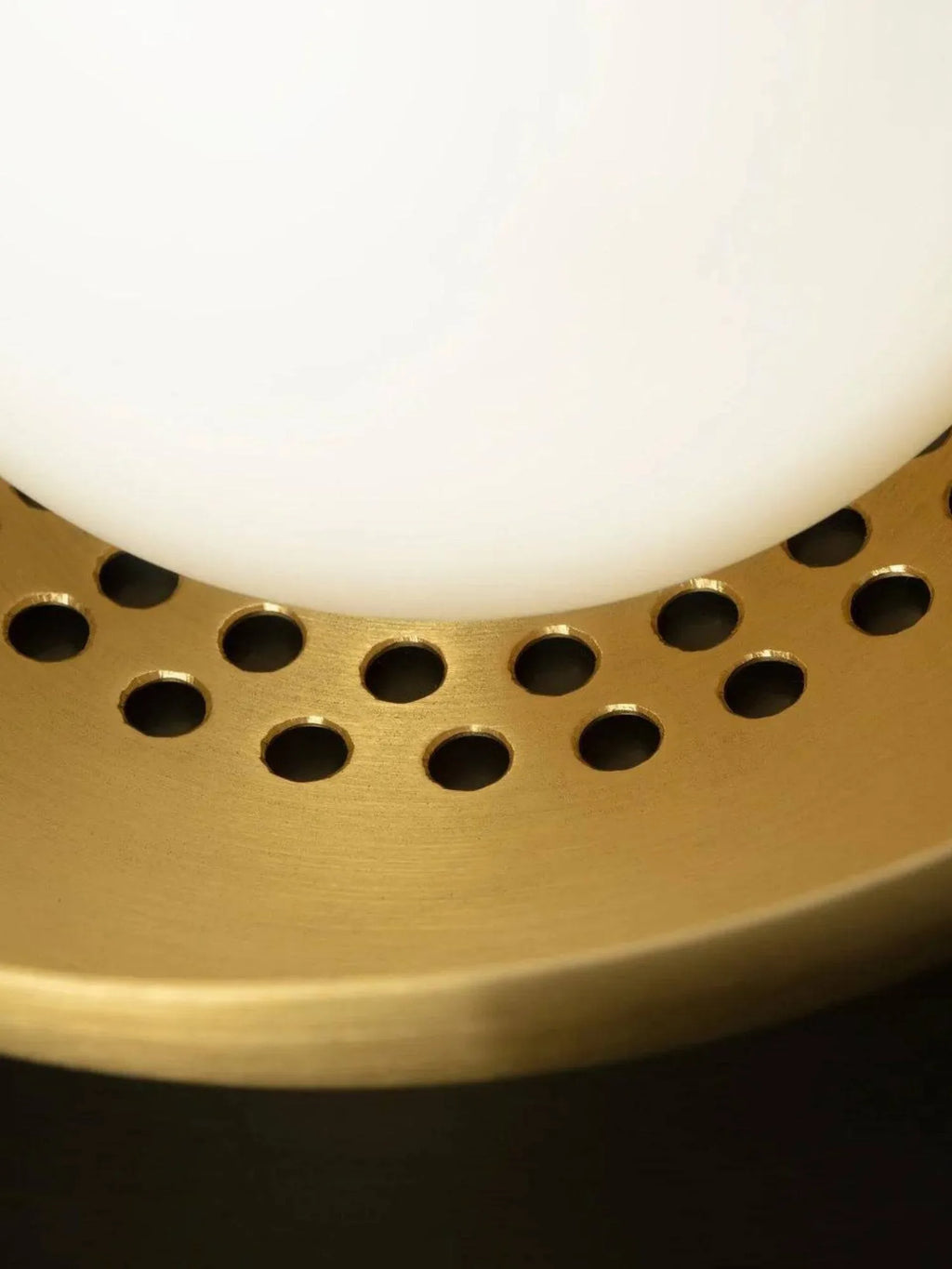 CTO Lighting Carapace Ceiling Lamp, a luxurious contemporary flush mount light featuring a warm brushed brass frame with a distinctive perforated design and a smooth white opal glass diffuser. The intricate circular perforations cast a unique glow, highlighting the rich golden brass finish and clean lines, embodying a sophisticated modern aesthetic. Perfect as a statement piece for luxury living rooms, elegant dining areas, or modern bedrooms seeking a touch of refined Art Deco-inspired lighting.