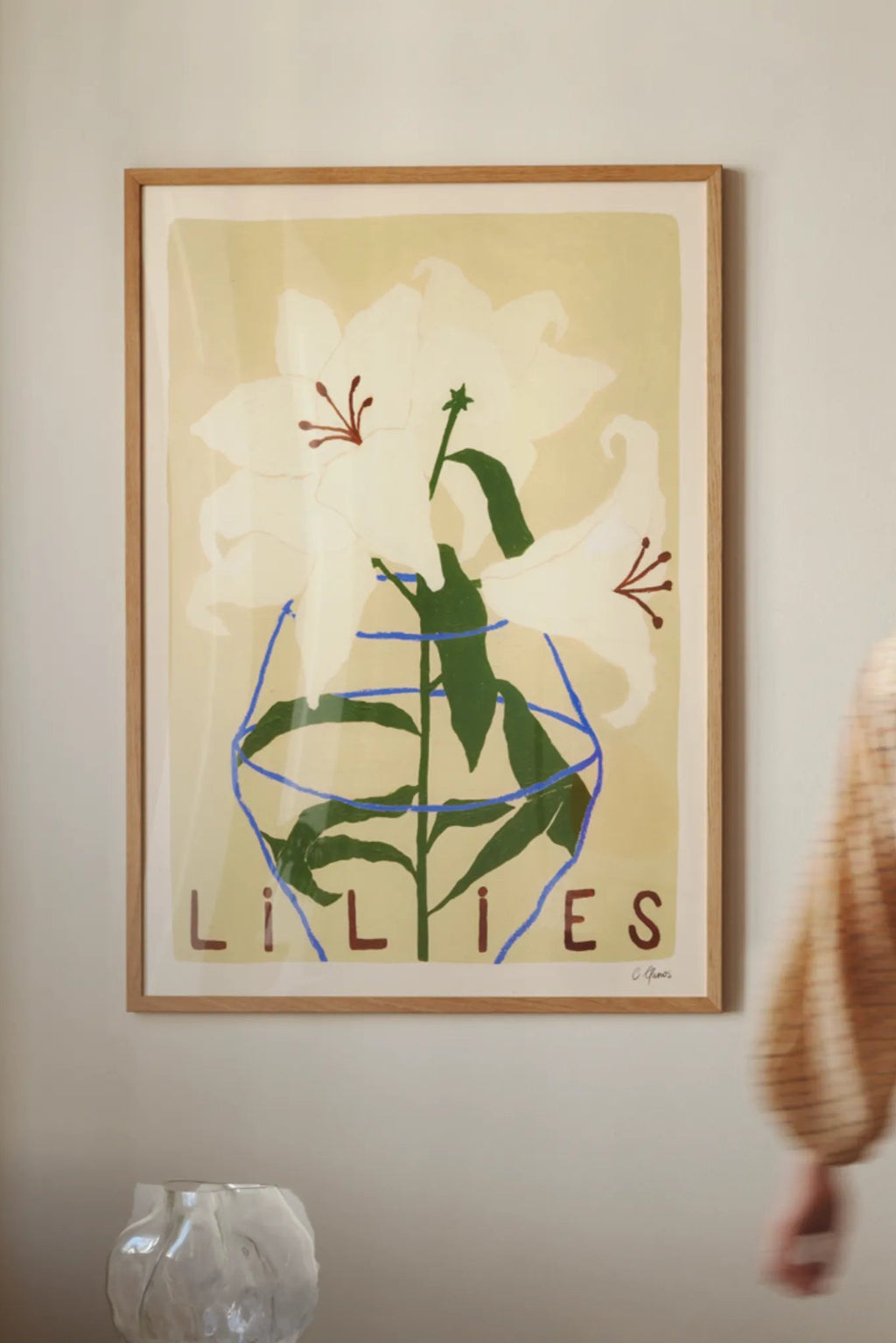 The Poster Club Lilies, a modern botanical art print featuring abstract white lilies with dark green stems and red-brown stamens, set against a pale yellow background with a blue abstract vase outline and "LILIES" text. Framed in natural oak, this contemporary floral poster is perfect for Scandinavian living rooms or minimalist gallery walls.