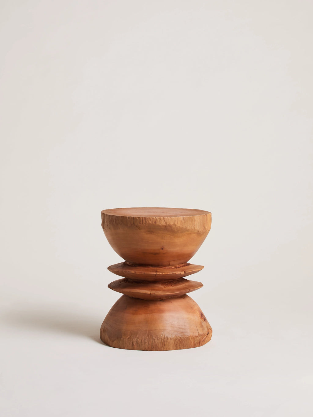 Heaps & Woods Caro Stool, a sculptural solid wood stool hand-carved from natural wood with warm, varied grain and a rustic, organic modern aesthetic. Its unique hourglass silhouette features a flat round top, a bowl-shaped upper, and two stacked disc-like elements leading to a rounded base. This versatile accent piece is perfect as a side table or statement stool for contemporary living rooms, wabi-sabi bedrooms, or natural minimalist entryways.