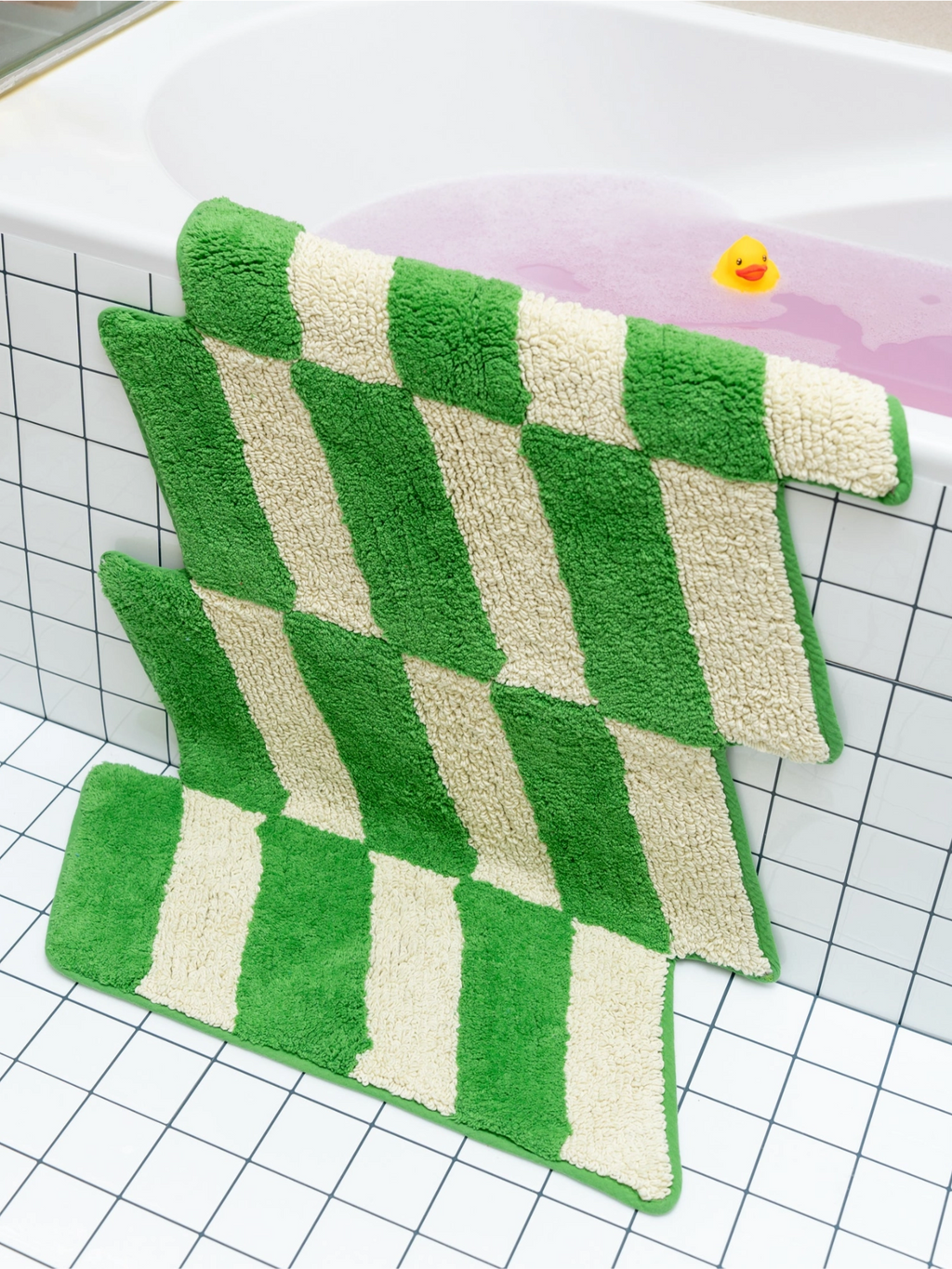 TARTA GELATINA Cassette Bath Mat, a playful tufted cotton bath mat featuring a bold bright green and cream wavy checkerboard pattern with an irregular, zig-zag shape and plush texture. This fun, graphic bath mat is perfect for adding a retro-inspired accent to modern bathrooms or contemporary spaces.